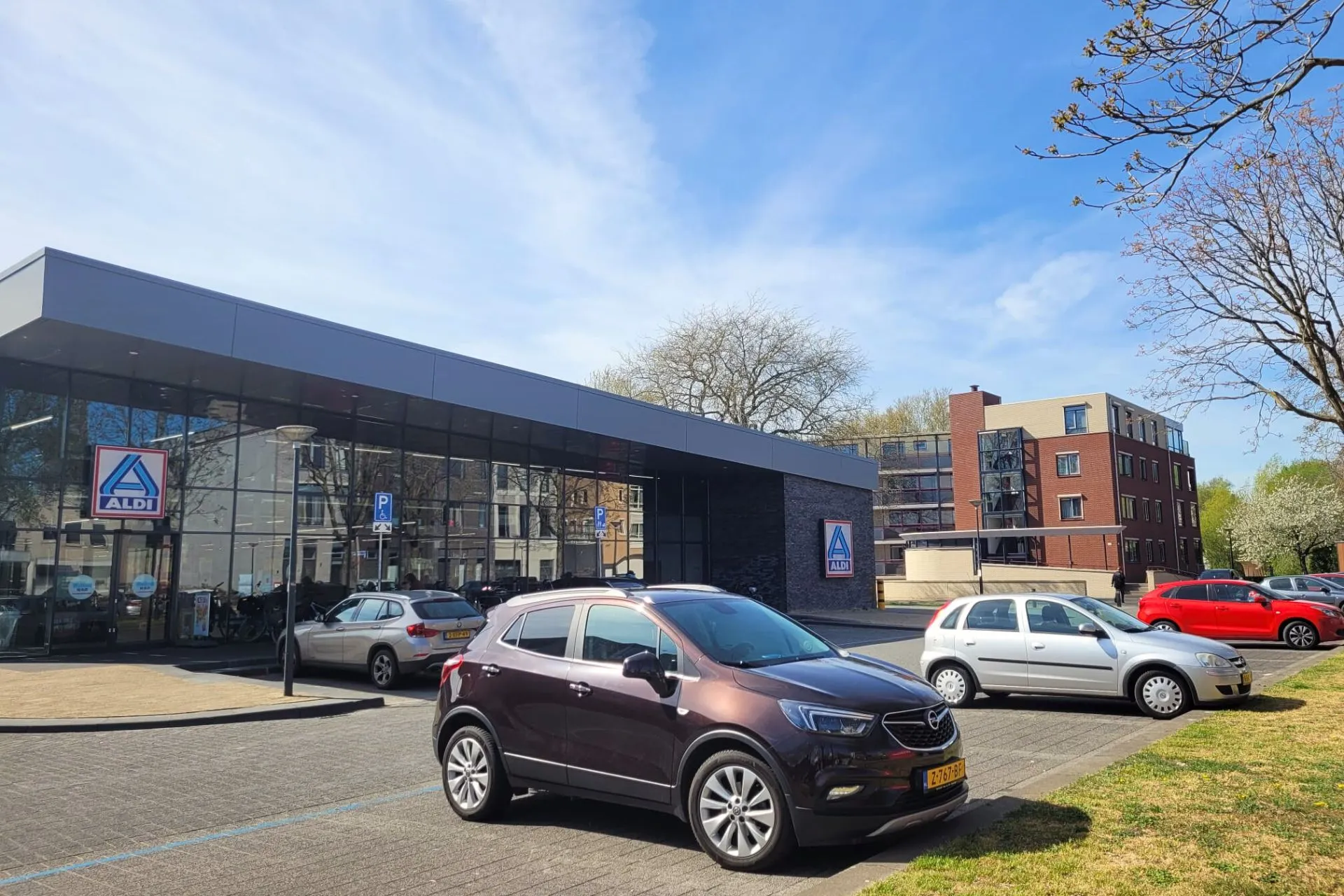Parkeerplaats bij de Aldi in Veghel op een zonnige dag met blauwe lucht; een rij met parkeerplaatsen waar je 2 uur mag parkeren met een blauwe schijf. Vanaf hier is het 2 minuten lopen naar Travelcenter de Wit Veghel.