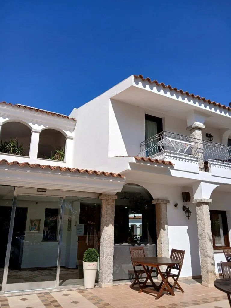 Verblijf in San Teodoro, wit huisje met balkon en houten tuinsetje.