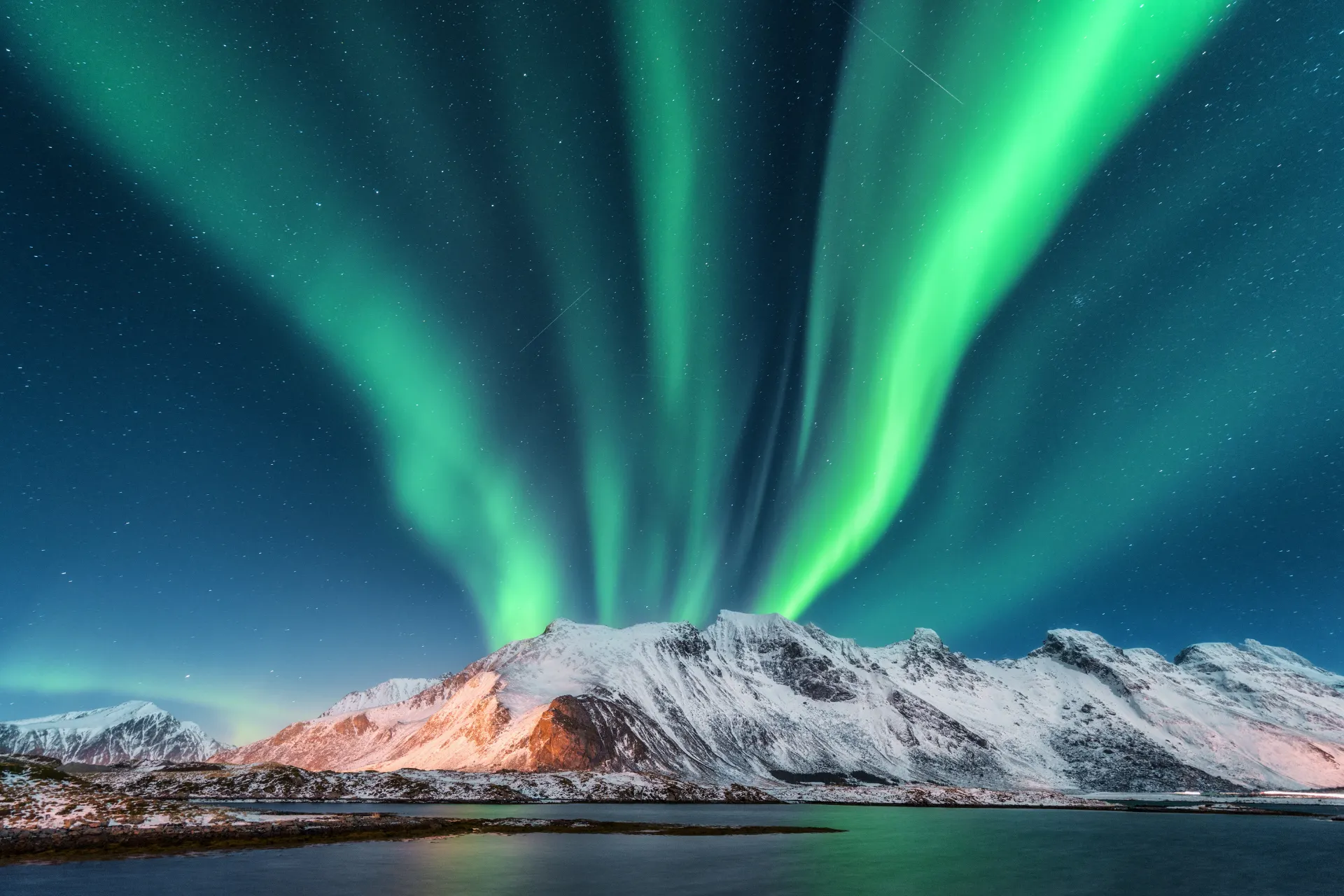 Noorderlicht boven een berglandschap in Noorwegen met heldergroene lichtgolven aan de hemel.