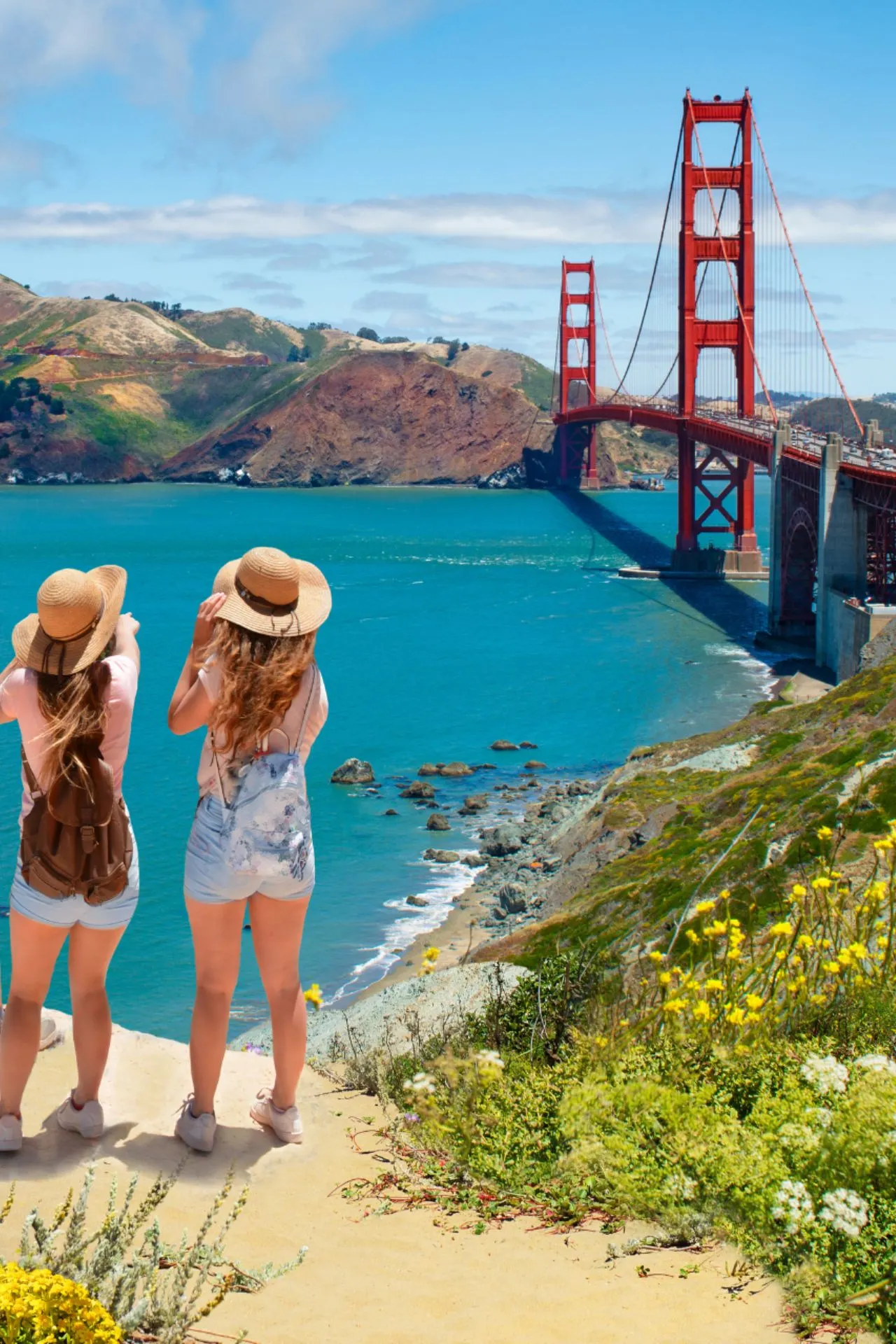 Twee reizigers met strohoeden en rugzakken bewonderen het uitzicht op de iconische Golden Gate Bridge in San Francisco, Californië, omringd door kleurrijke wilde bloemen en een helderblauwe zee.