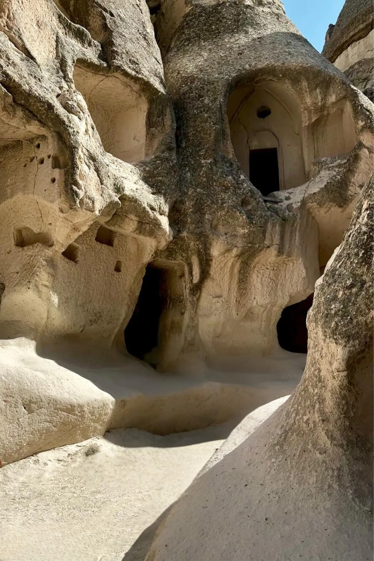 Detail van een uitgehouwen grot in Cappadocië, Turkije, met zachte vulkanische rotsen die door eeuwenlange erosie en menselijke hand zijn gevormd. De natuurlijke vormen en openingen leiden naar donkere kamers en gangen, ooit gebruikt als woningen of kerken. Het zonlicht benadrukt de textuur van het gesteente en creëert een mystieke sfeer. Deze historische plek is een belangrijk onderdeel van het UNESCO-werelderfgoed en een populaire bestemming voor cultuur- en geschiedenisliefhebbers die unieke architectuur willen ontdekken.