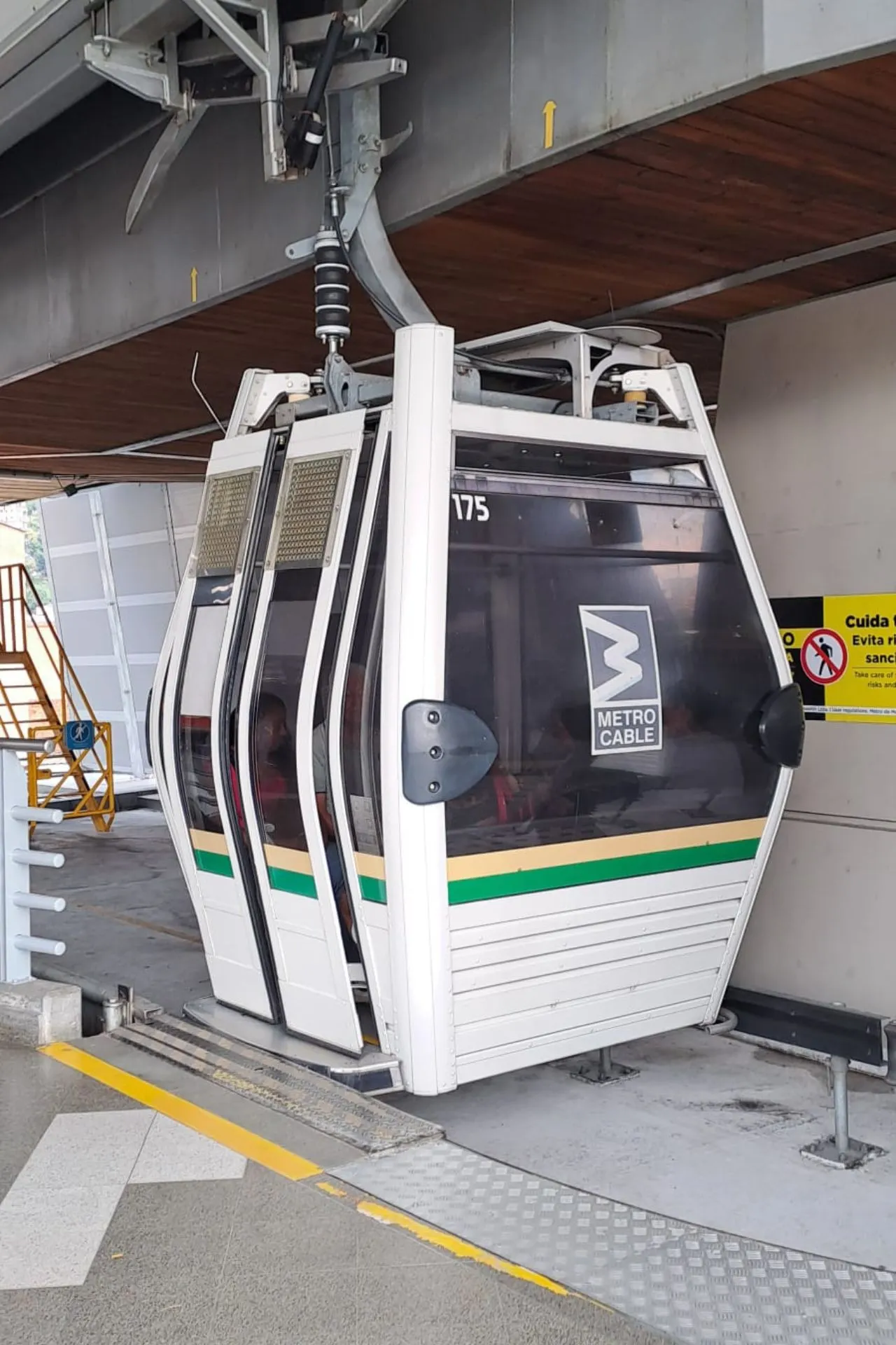 Witte gondel van het MetroCable-systeem in Medellín, bevestigd aan een kabelbaanstation met metalen en houten constructie.