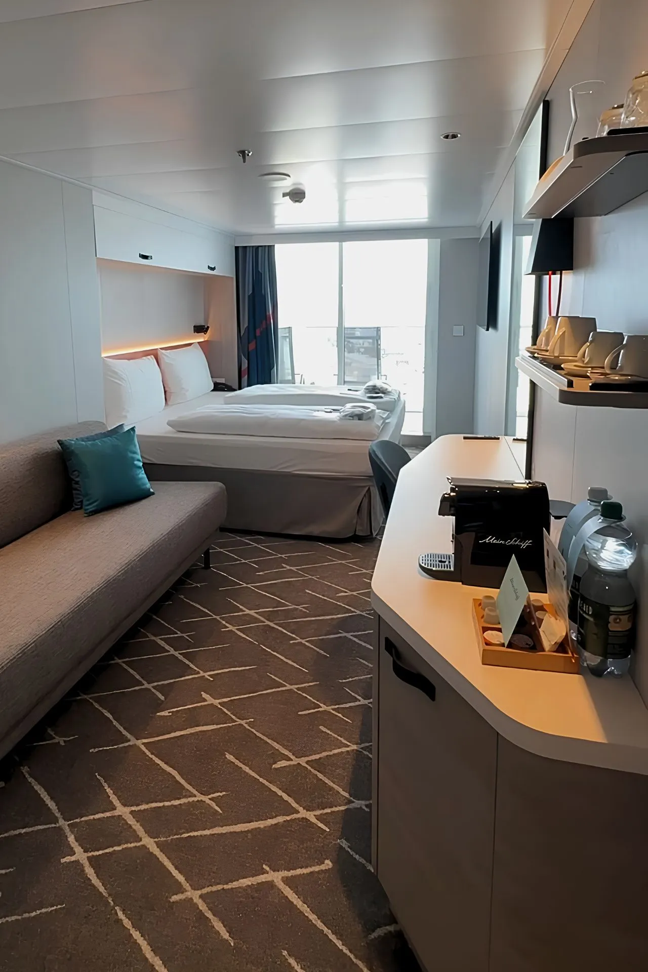 Ruime en moderne balkonhut aan boord van de Mein Schiff Flow met comfortabel tweepersoonsbed, zithoek, bureau en koffievoorzieningen. Door de grote glazen deuren valt veel daglicht binnen en heb je direct toegang tot het privébalkon. De stijlvolle inrichting en slimme indeling zorgen voor een ontspannen verblijf tijdens een cruise.