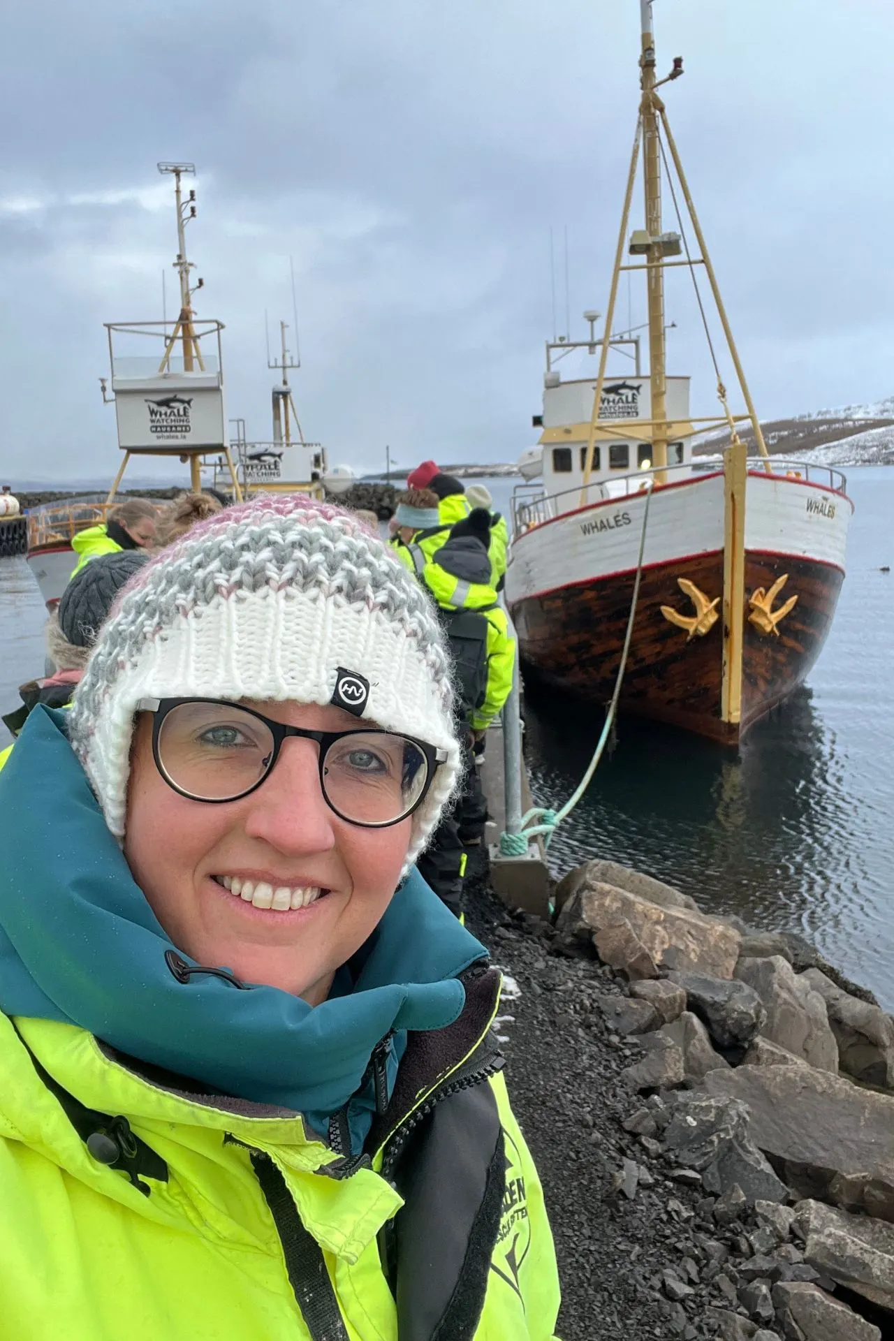 Walvissafariboot aangemeerd aan de steiger in Hauganes, Noord‑IJsland, met reizigers in gele overalls.
