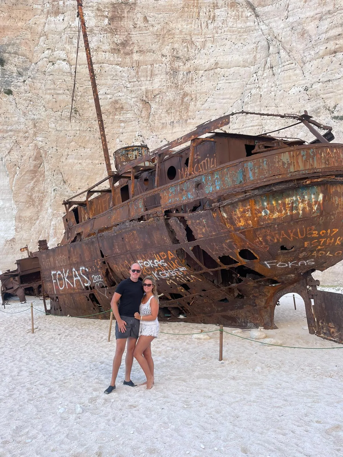 Blonde vrouw en haar partner poseren voor het wrak op Shipwreck Beach in Zakynthos, Griekenland.