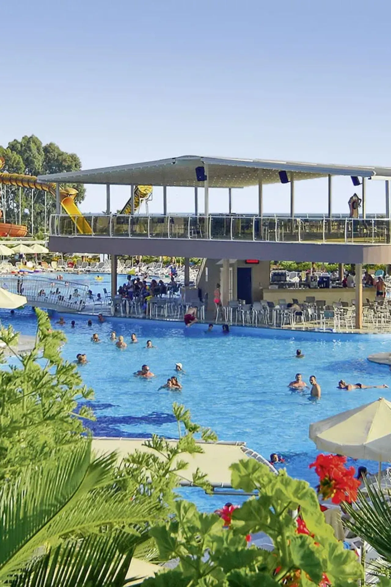 Een groot waterpark met kleurrijke glijbanen, waaronder een opvallende slangvormige glijbaan. Voor de glijbanen ligt een ruim zwembad met ligbedden rondom.