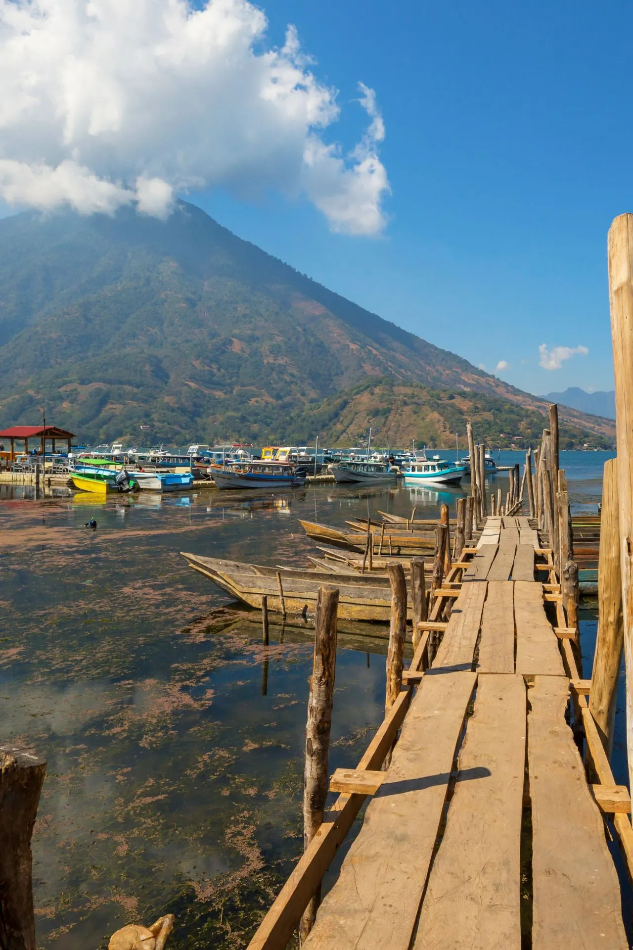 Houten aanlegsteiger met bootjes aan Lake Atitlán, met een vulkaan op de achtergrond in Guatemala.
