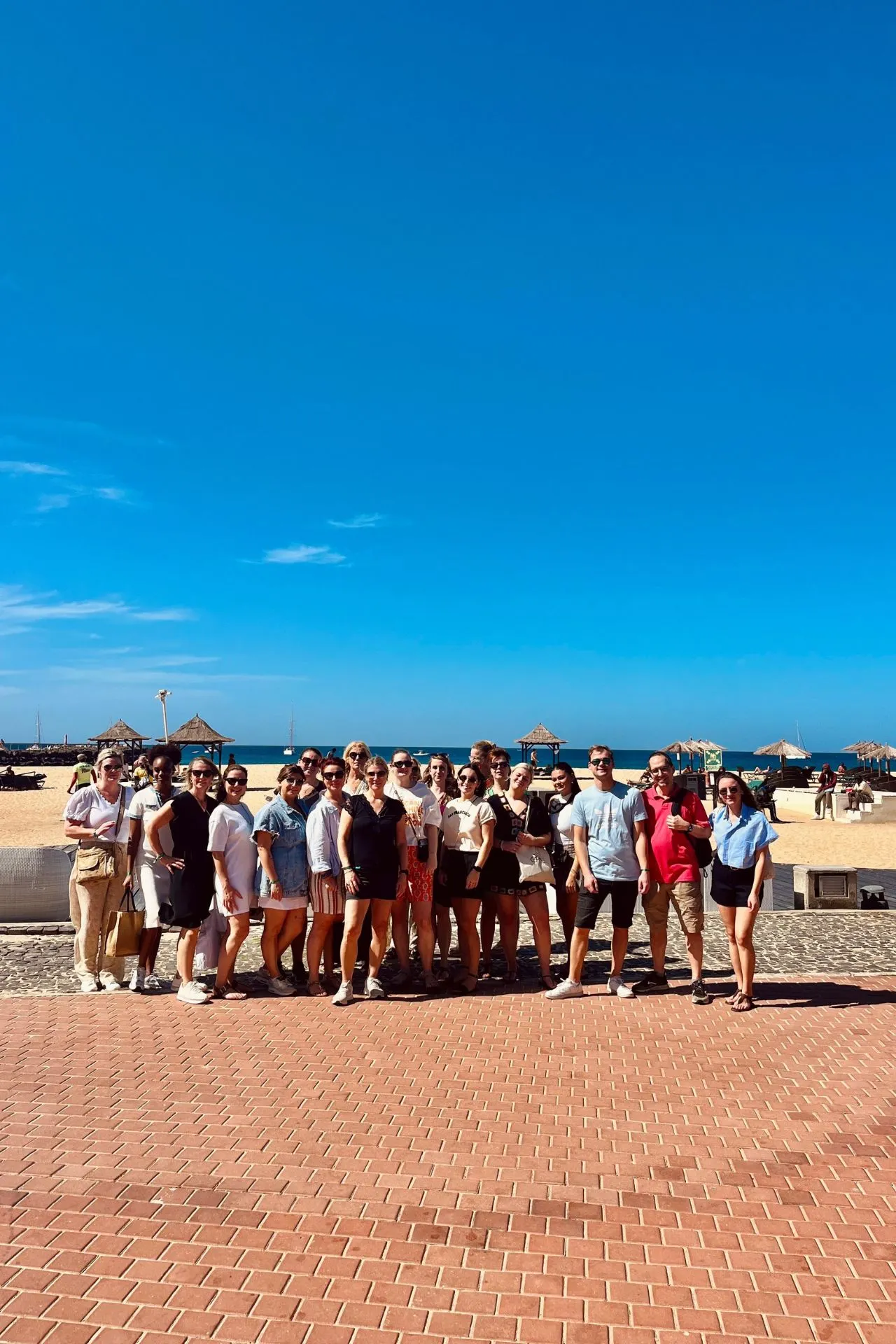 Groepsfoto op een zonnige promenade aan zee op Kaapverdië, met palmbomen, strandparasols en de Atlantische Oceaan op de achtergrond. Deze setting laat perfect zien hoe ontspannen en sociaal een vakantie Kaapverdië kan zijn, met veel ruimte voor strandbeleving en gezamenlijke momenten. Voor reizigers die een georganiseerde reis Kaapverdië overwegen, benadrukt dit beeld de combinatie van zon, zee en informele sfeer die vooral populair is op eilanden zoals Sal en Boa Vista.

