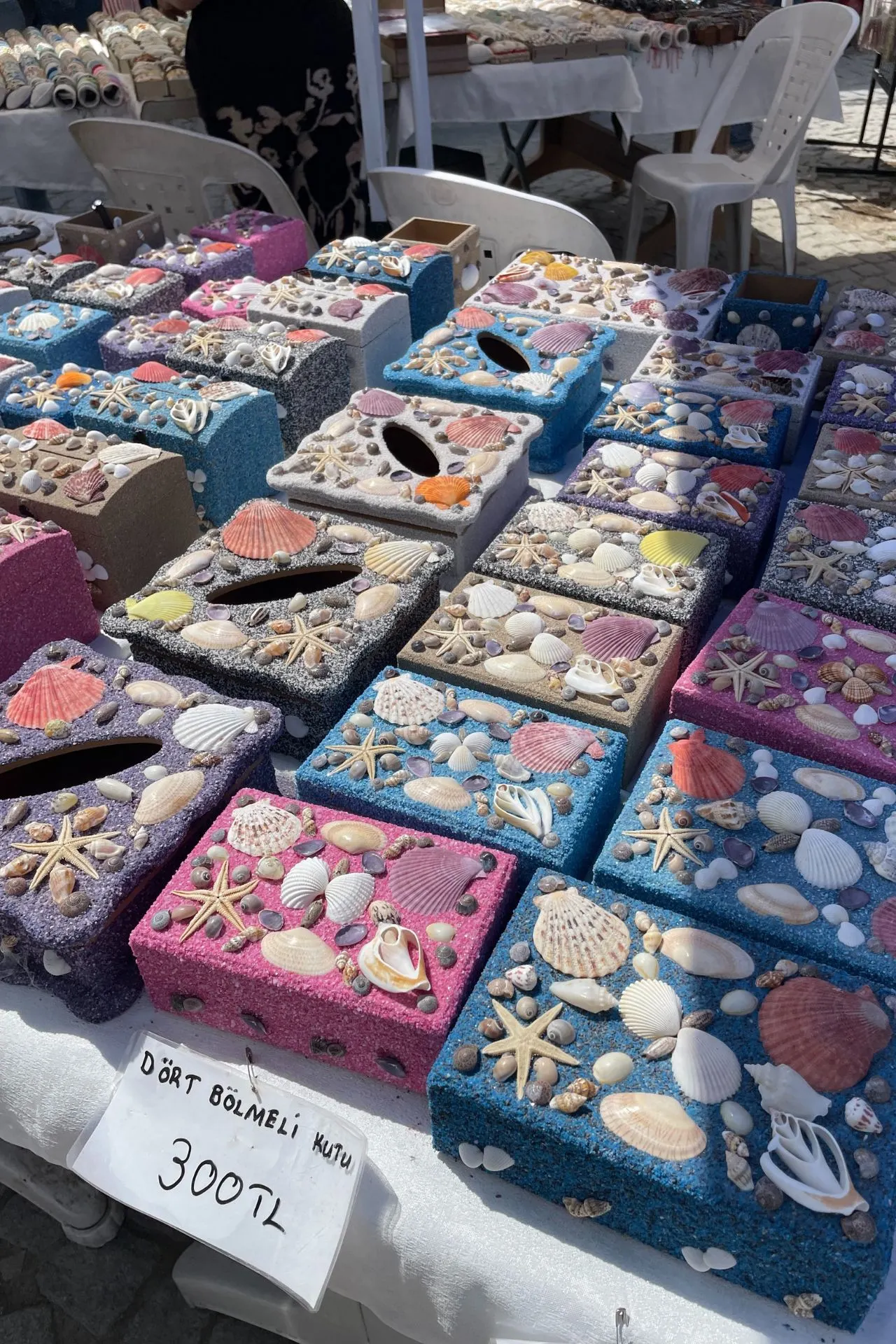 Kleurrijke handgemaakte doosjes versierd met schelpen, zeesterren en steentjes op een marktkraam in Sığacık.