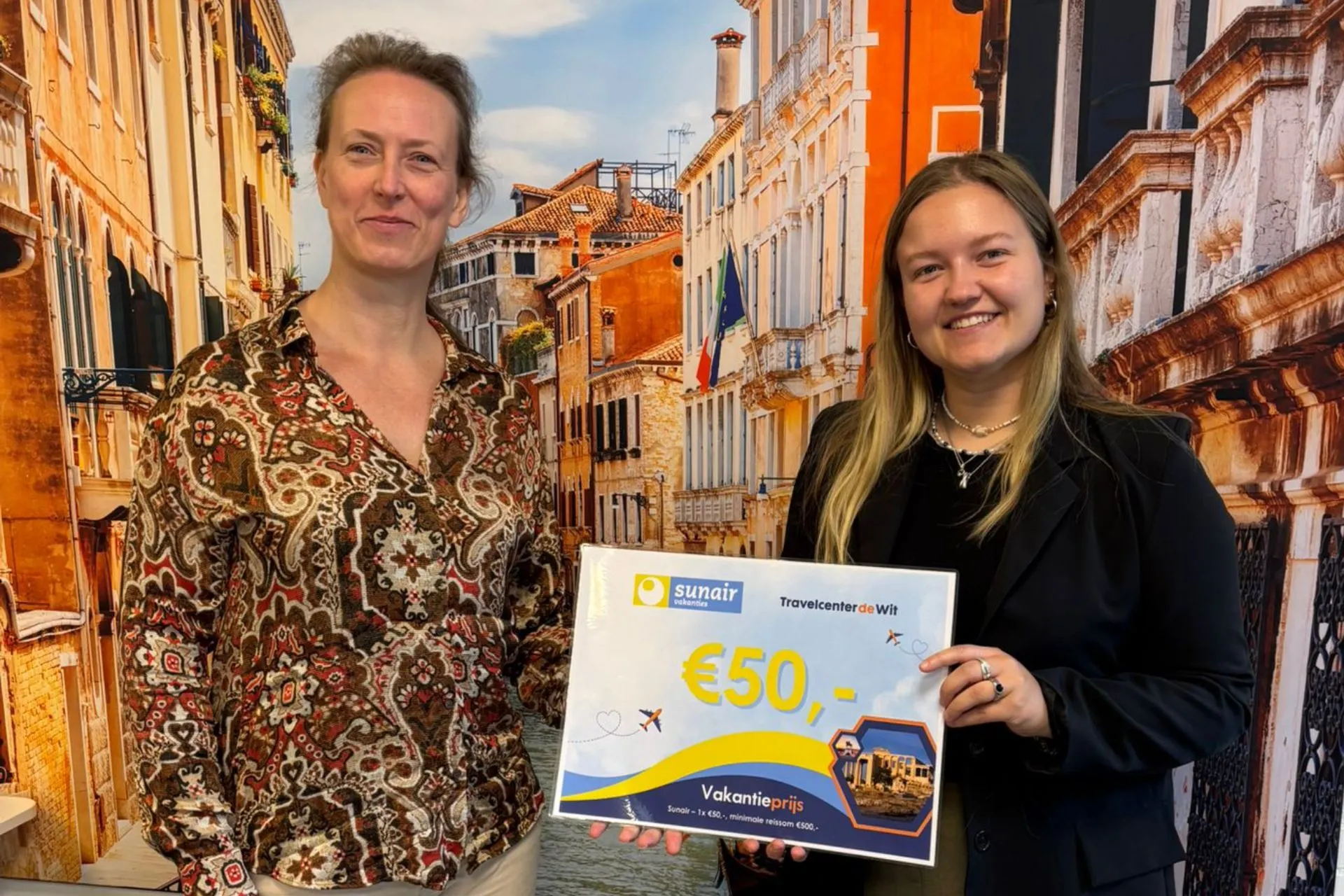 Twee vrouwen poseren met een Sunair-voucher van €50 tijdens de prijsuitreiking van de winactie bij Travelcenter de Wit Gemert.
