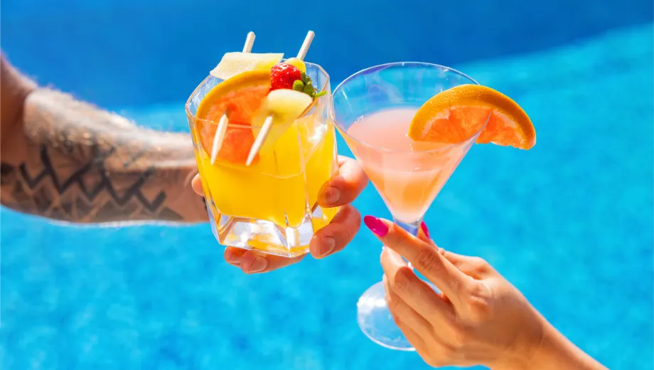 "Twee kleurrijke cocktails bij een helderblauw zwembad, één tropische gele cocktail met fruitgarnering en één roze cocktail met een schijfje sinaasappel. Perfecte setting voor luxe vakantie, ontspanning en zomerse sfeer. Ideaal voor poolside drinks, zonvakantie en mediterrane lifestyle. Ontdek verfrissende cocktails, relaxmomenten en het ultieme vakantiegevoel in een zonnige bestemming."