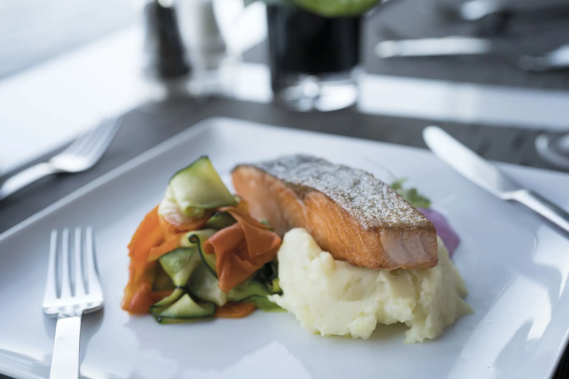 Netjes gepresenteerd bord met zalm, groenten en aardappelpuree, geserveerd aan boord van het luxe cruiseschip Emerald Destiny met uitzicht op de rivier en een stijlvolle tafelschikking.