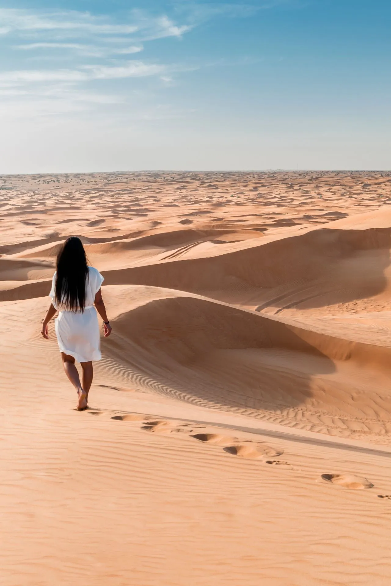 Indrukwekkend beeld van een uitgestrekte woestijn met golvende zandduinen onder een heldere blauwe lucht. Op de voorgrond loopt een persoon in een witte outfit op blote voeten door het warme zand, waarbij duidelijke voetafdrukken achterblijven. Dit landschap straalt rust en avontuur uit en is typerend voor bestemmingen zoals Dubai, een van de beste winterzon bestemmingen voor reizigers die op zoek zijn naar zon, warmte en unieke ervaringen. Terwijl in Europa de winter heerst, biedt deze plek een perfecte zonvakantie in december of een zonvakantie in januari, met temperaturen die vaak boven de 25 graden liggen. Voor iedereen die zich afvraagt: waar is het warm in januari? De woestijn van Dubai is het antwoord. Naast luxe resorts en moderne architectuur, biedt deze bestemming ook authentieke ervaringen zoals woestijnsafari’s, kamelenritten en spectaculaire zonsondergangen. Het zachte zand en de eindeloze horizon maken deze plek ideaal voor fotografie, ontspanning en avontuur. Ontdek waarom zoveel reizigers Dubai kiezen als een van de beste winterzon bestemmingen en plan jouw perfecte zonvakantie in december of januari op een locatie waar het altijd warm, zonnig en exotisch is. Deze foto straalt vrijheid, natuur en ultieme vakantiesfeer uit – alles wat je zoekt voor een onvergetelijke winterzon ervaring.
