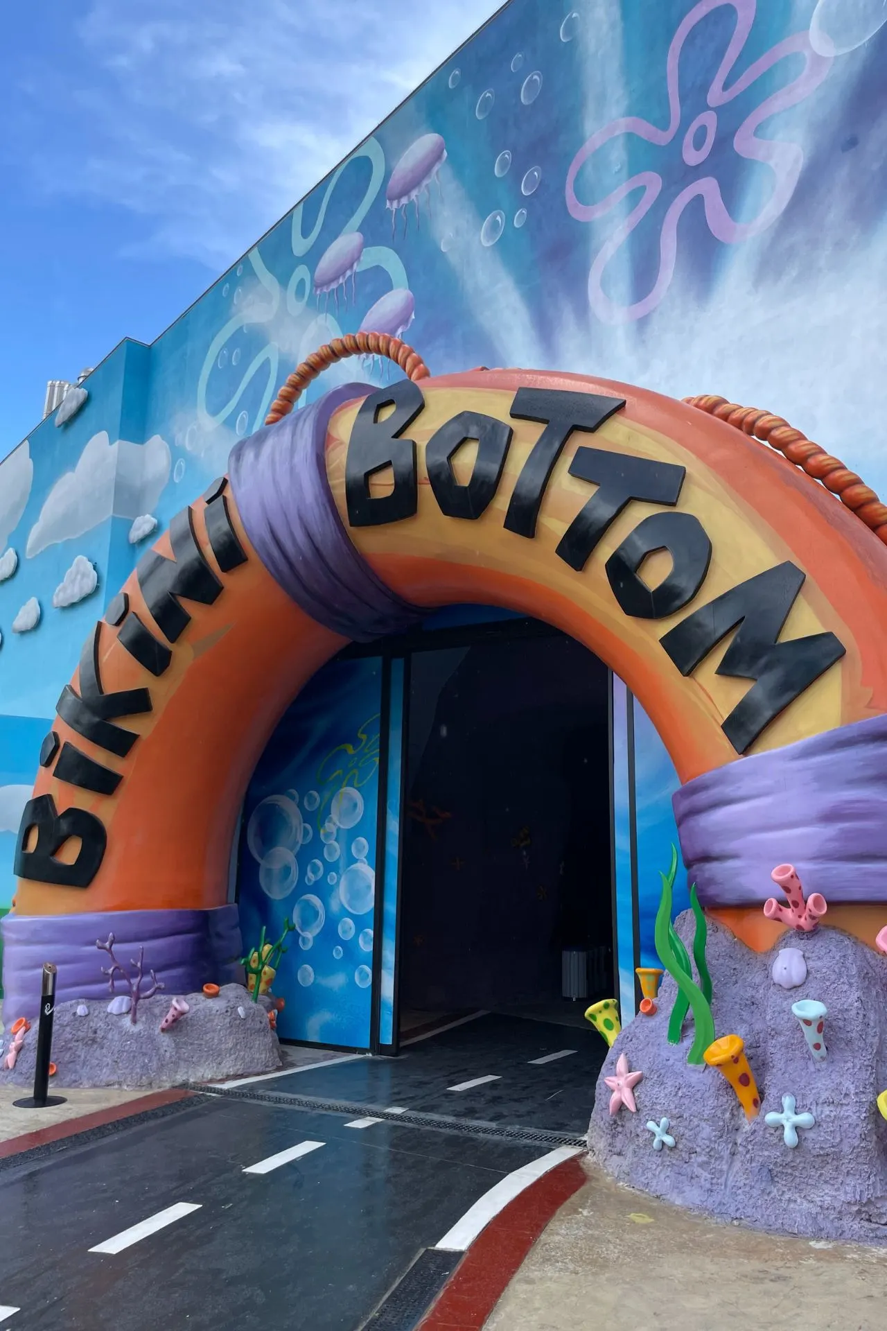 Speelse ingang in de vorm van een grote oranje reddingsboei met de tekst “Bikini Bottom”, omringd door decoratieve zeedieren.
