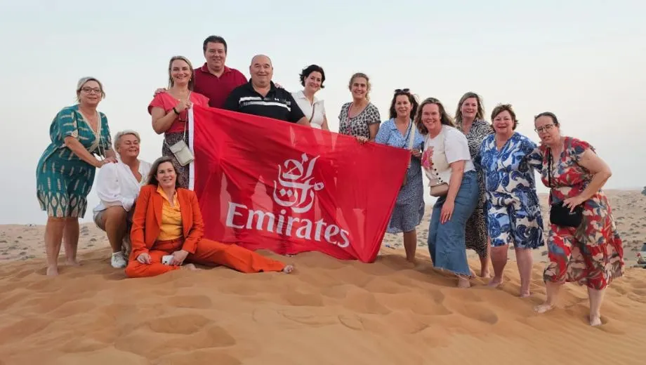 Groepsfoto van reisadviseurs met een rode Emirates-vlag, poseren in de duinen van Ras Al Khaimah.