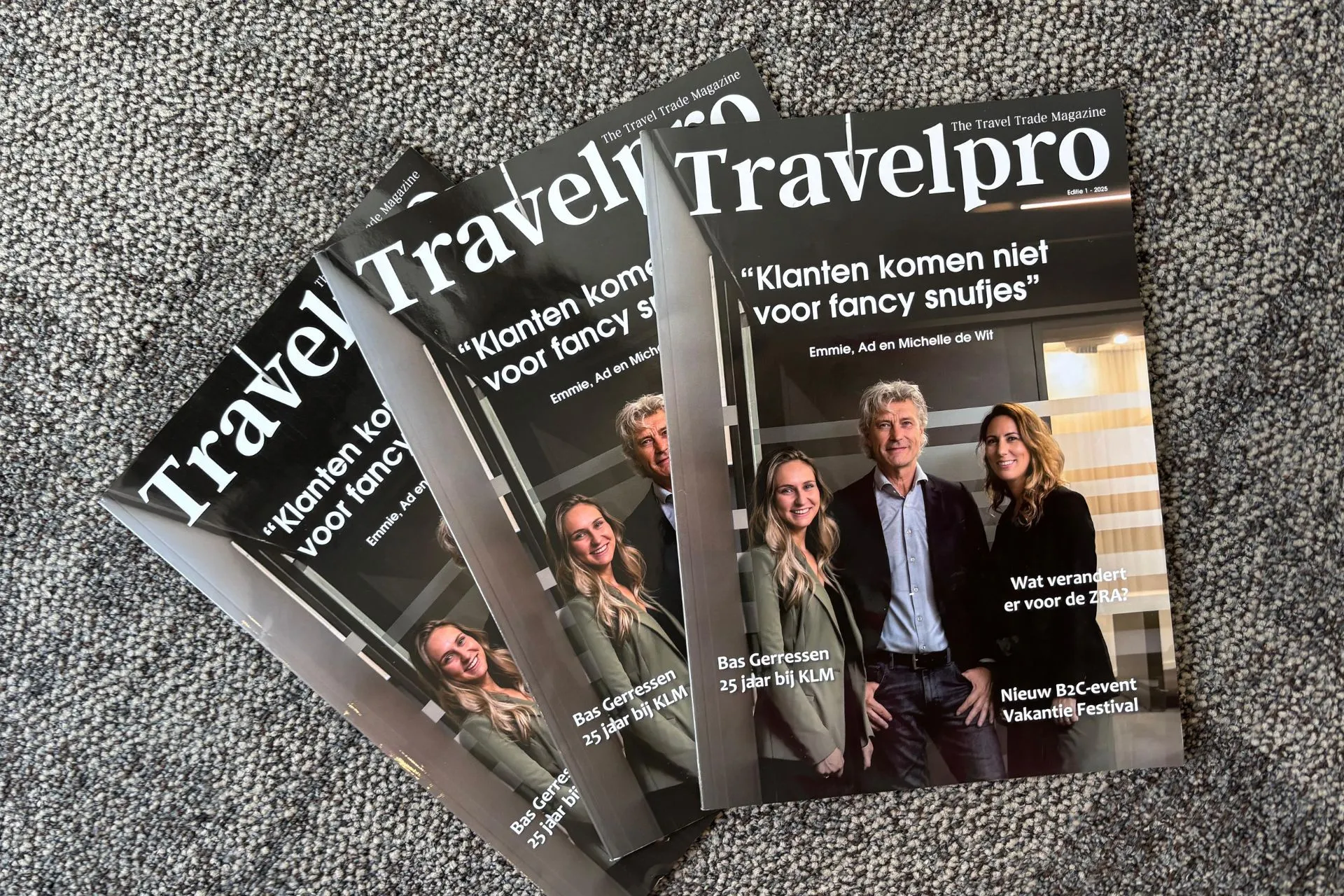 Drie Travelpro-magazines met Emmie, Ad en Michelle op de covers liggen als een waaier naast en over elkaar op een donkerkleurig tapijt. 