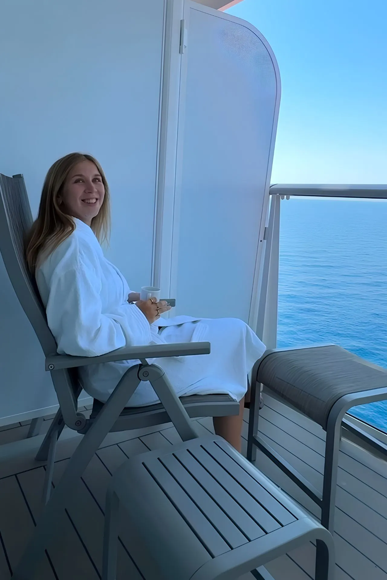 Marketeer Martje op het privébalkon van een hut aan boord van de Mein Schiff Flow, zittend in een comfortabele loungestoel met uitzicht op de kalme zee. Deze foto laat de rust, ruimte en ontspannen sfeer zien die een cruisevakantie biedt, terwijl de reis zelf onderdeel wordt van de ervaring.