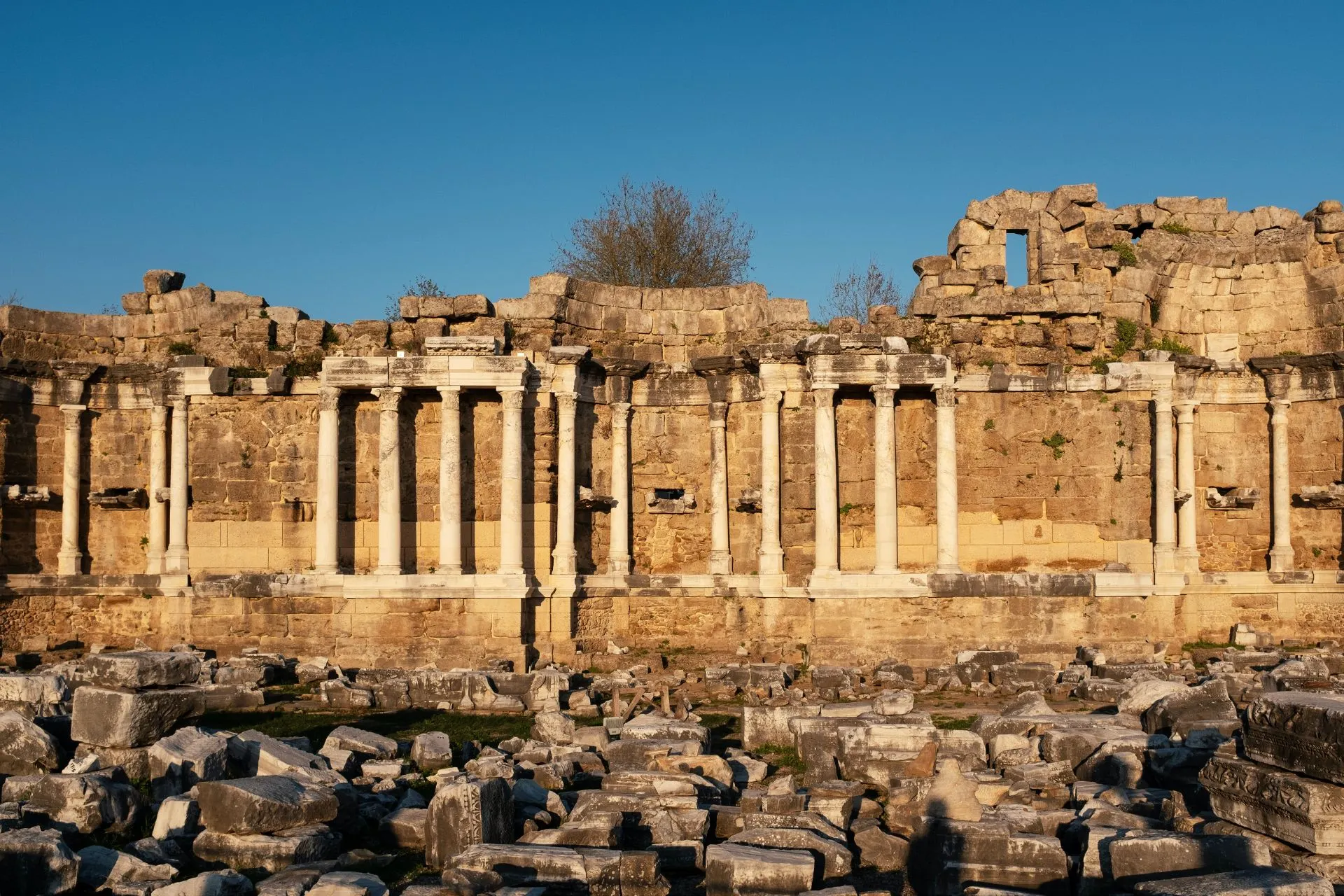 Historische ruïnes van het oude Side aan de Turkse Rivièra, met een indrukwekkende rij marmeren zuilen, eeuwenoude stenen muren en verspreide archeologische resten op de voorgrond. Deze bijzondere opgravingen behoren tot de belangrijkste bezienswaardigheden van Side en bieden een fascinerende inkijk in de rijke geschiedenis van deze populaire vakantiebestemming in Turkije.Geef uw feedback over BizChat