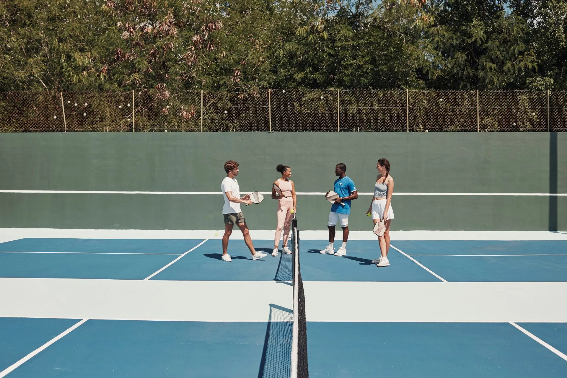 Club Med all-inclusive resort met sportactiviteiten: vier gasten spelen tennis op een moderne tennisbaan omringd door groen. Geniet van actieve vakanties met tennis, yoga en watersporten bij Club Med in Europa, Caraïben of Azië.
