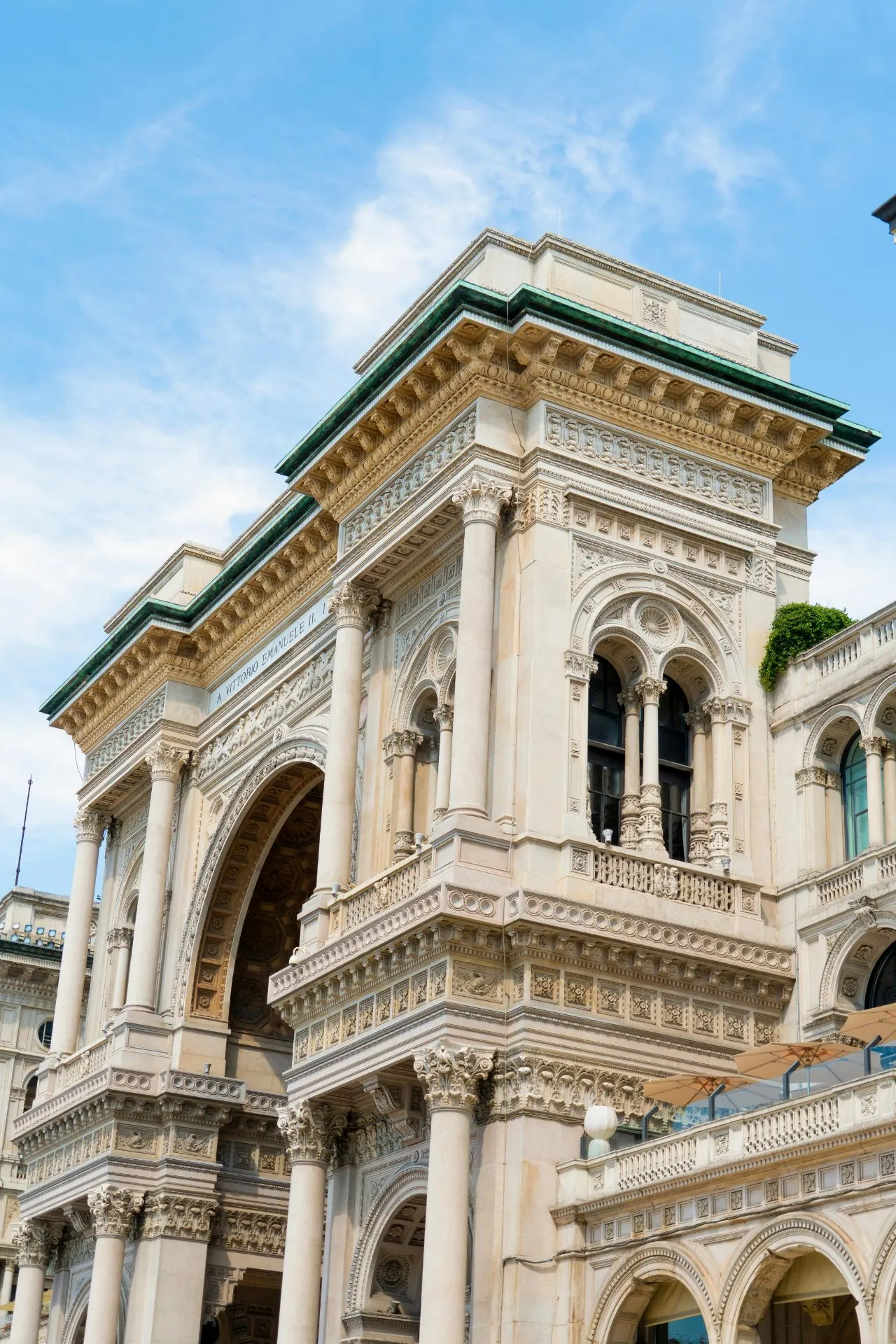 De monumentale toegangspoort tot de Galleria Vittorio Emanuele II in Milaan, met rijk versierde zuilen, bogen en geveldetails onder een heldere blauwe lucht.

