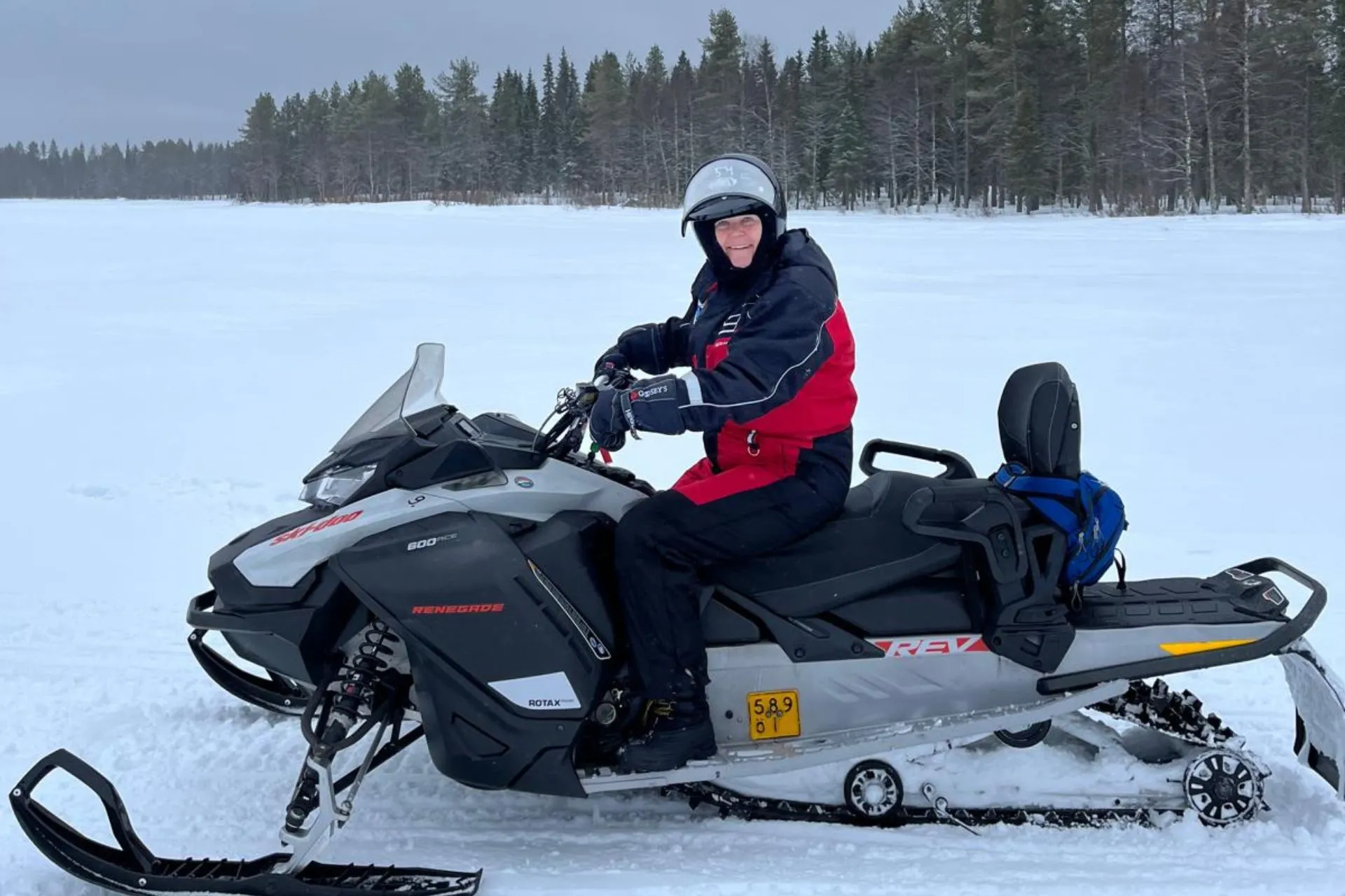 Persoon in rode winterkleding zit op een sneeuwscooter op een bevroren meer in Fins Lapland

