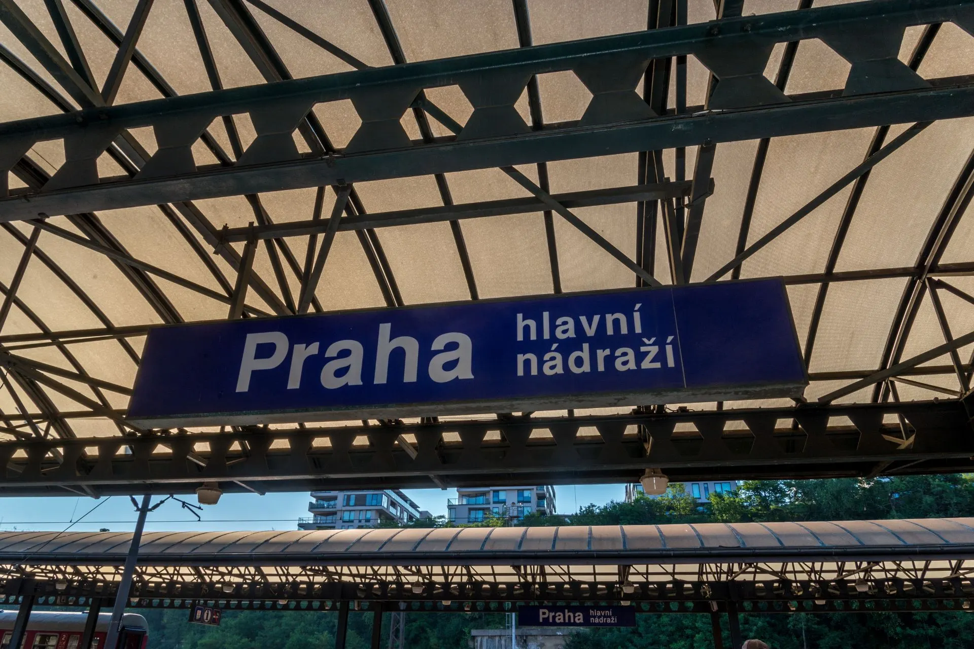 Bordje met de tekst 'Praha' dat aan het station van Praag hangt, tegen een achtergrond van het perron.