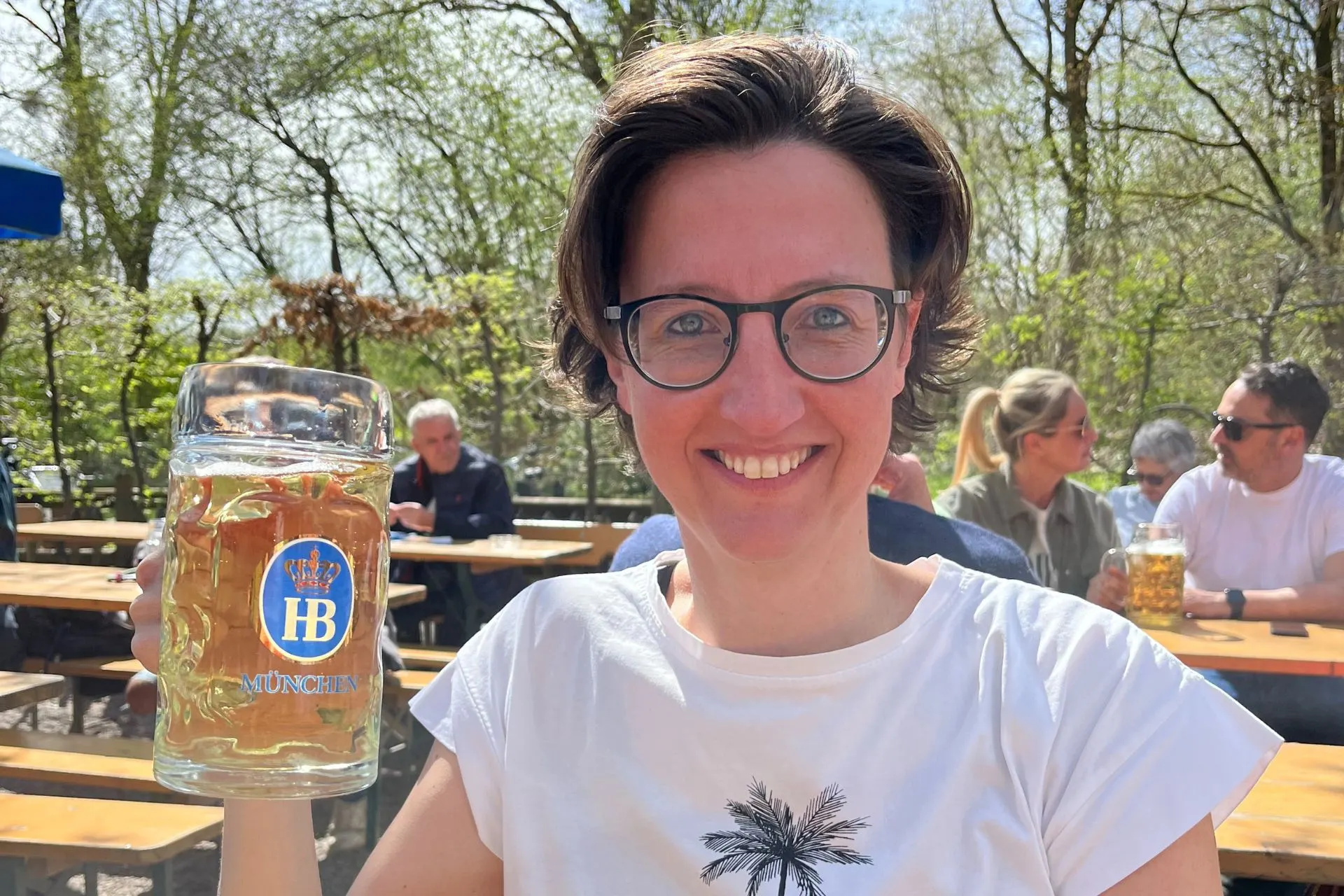 Een vrolijke vrouw, susan wolfs geniet van een grote pul bier in een traditionele Münchener Biergarten, omringd door gezelligheid en lentegroen.