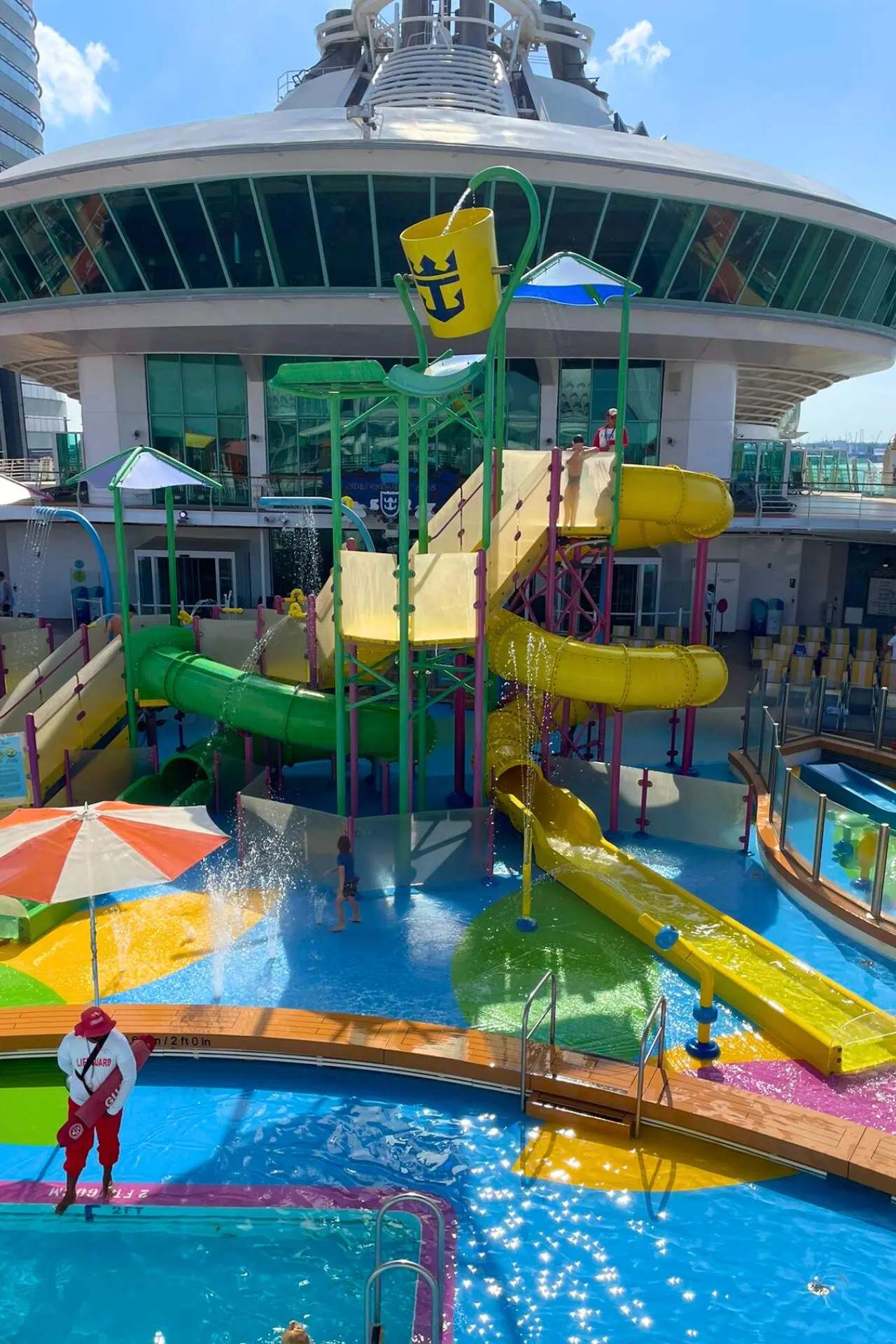 Waterpark voor kinderen op de Independence of the Seas, met meerdere glijbanen, een grote omkiepbak met het Royal Caribbean-logo en vrolijk spetterende fonteinen.