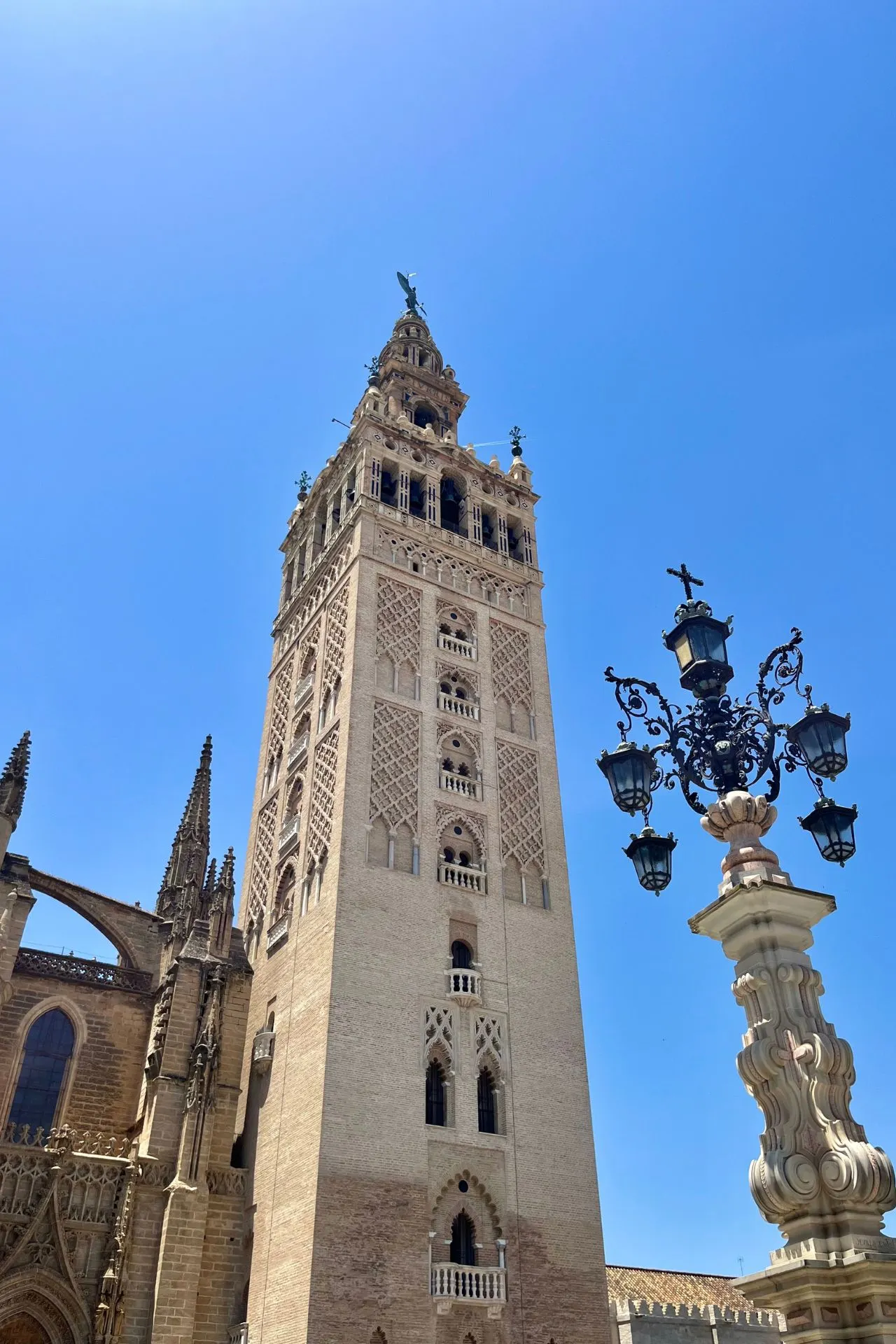 De Giralda, de klokkentoren van de Kathedraal van Sevilla, steekt imposant omhoog tegen een helderblauwe lucht. Rechts staat een sierlijke lantaarnpaal met smeedijzeren details.
