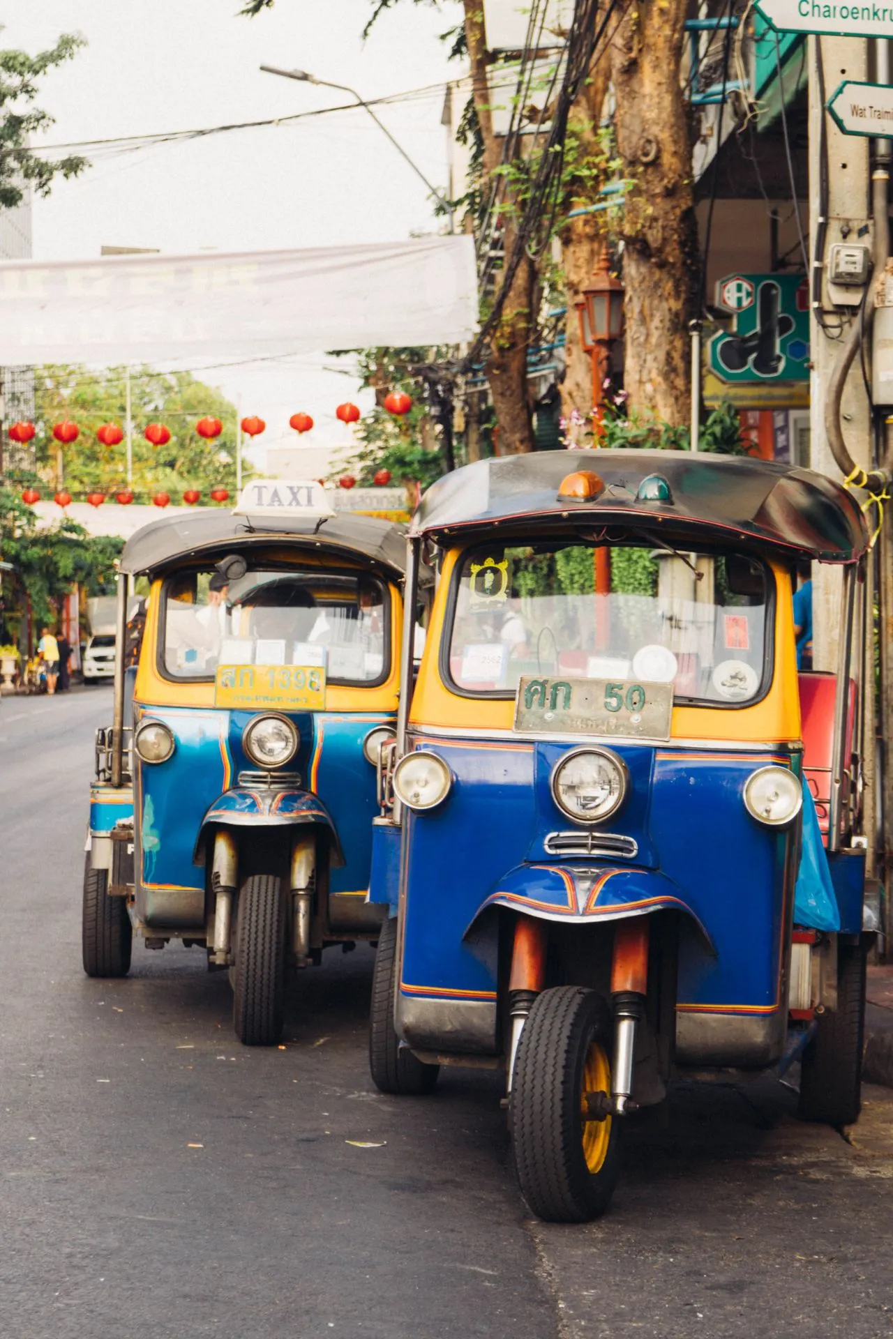Twee stilstaande tuktuks in geel en blauw, typisch voor Bangkok, staan geparkeerd op een drukke straat.