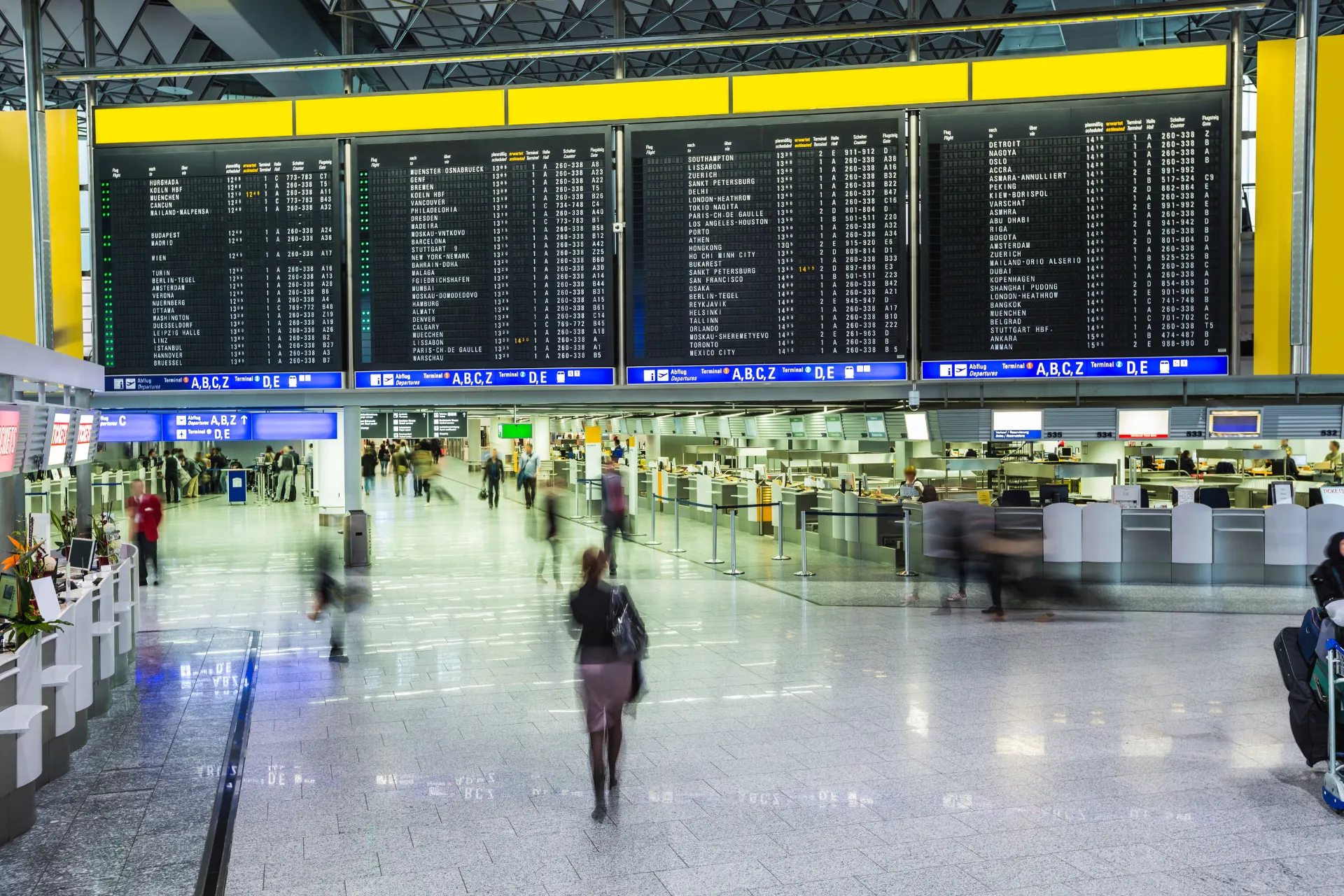  Drukke vertrekhal van Frankfurt Airport met grote digitale vertrekborden en bewegende passagiers.