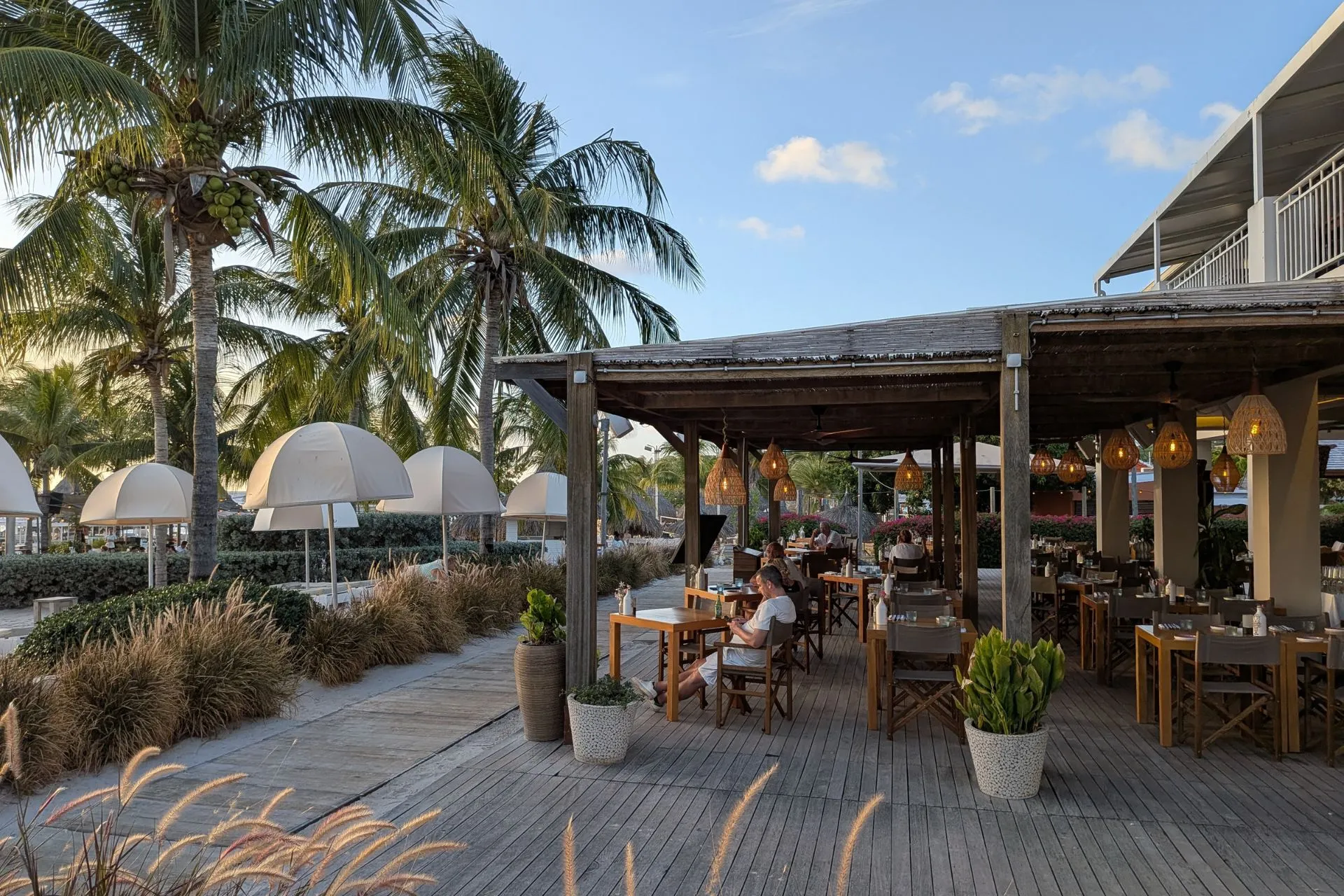 Gezellig openluchtrestaurant op Curaçao omringd door palmbomen en sfeervolle verlichting. Perfect voor een romantisch diner of ontspannen lunch met uitzicht op het strand. De houten tafels en tropische decoratie creëren een warme Caribische sfeer. Ideaal voor culinaire liefhebbers en vakantiegangers die genieten van lokale gastronomie.