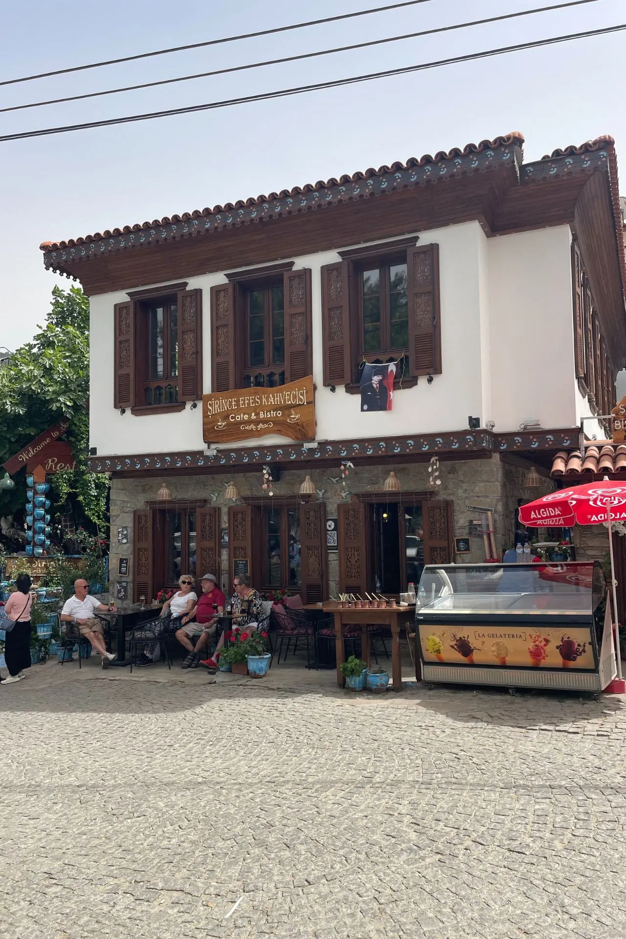 Traditioneel Turks huis met houten luiken in Şirince, met een terras vol bezoekers voor het café Şirince Efe's Kahvecisi.