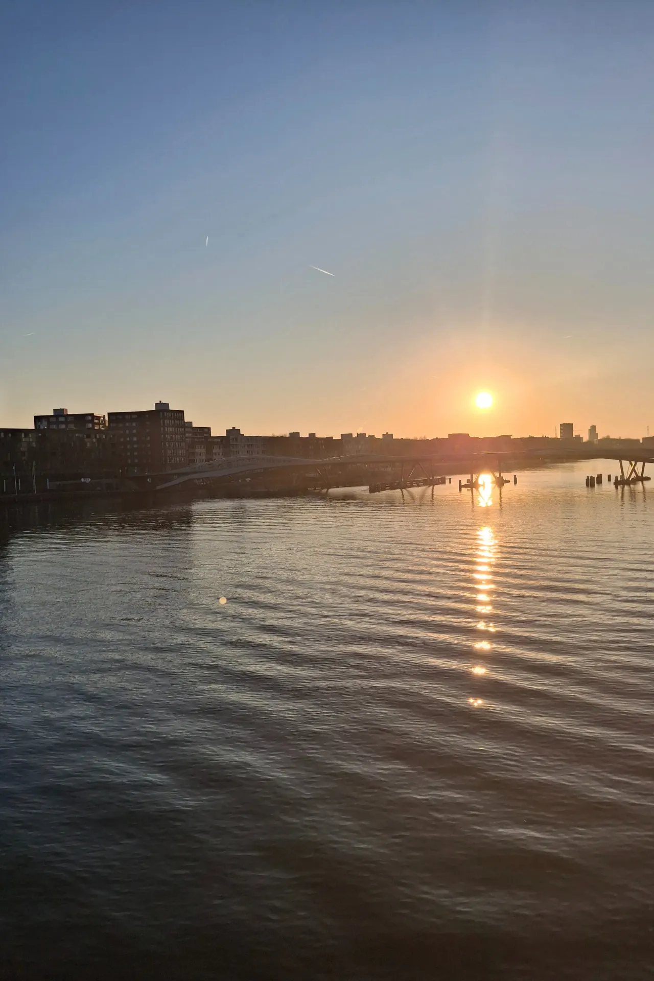 Zonsopkomst in Amsterdam gezien vanaf de Emerald Destiny, met warme ochtendkleuren weerspiegeld op het water.