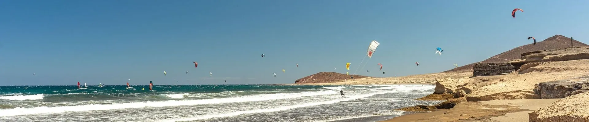 Kitesurfers op een breed strand met golven en ruig landschap aan de noordkust van het eiland
