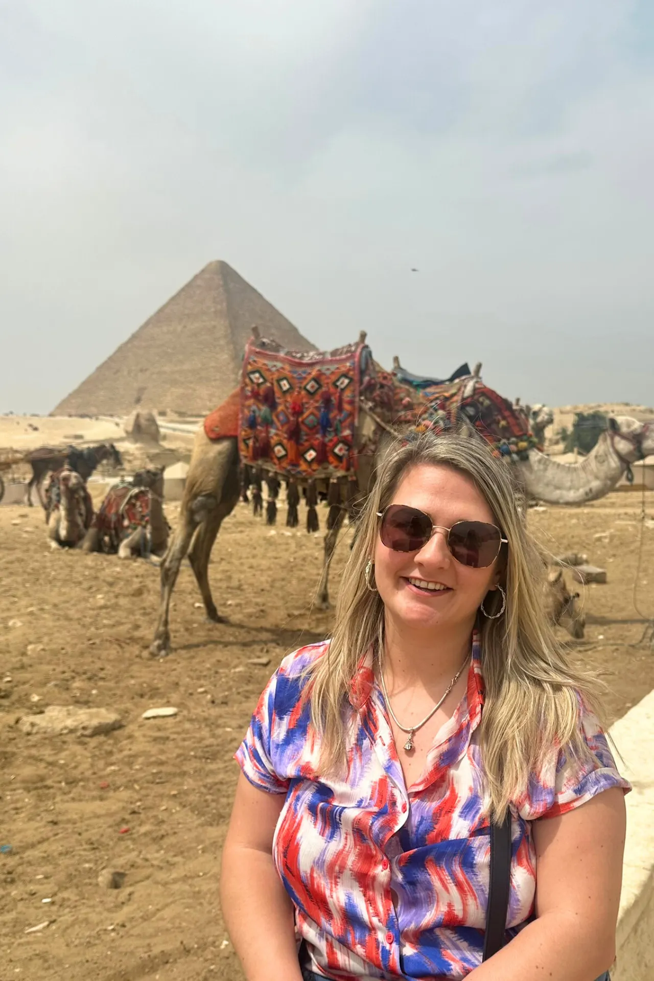 Naomi poseert lachend voor een piramide met een kameel op de achtergrond in Egypte.