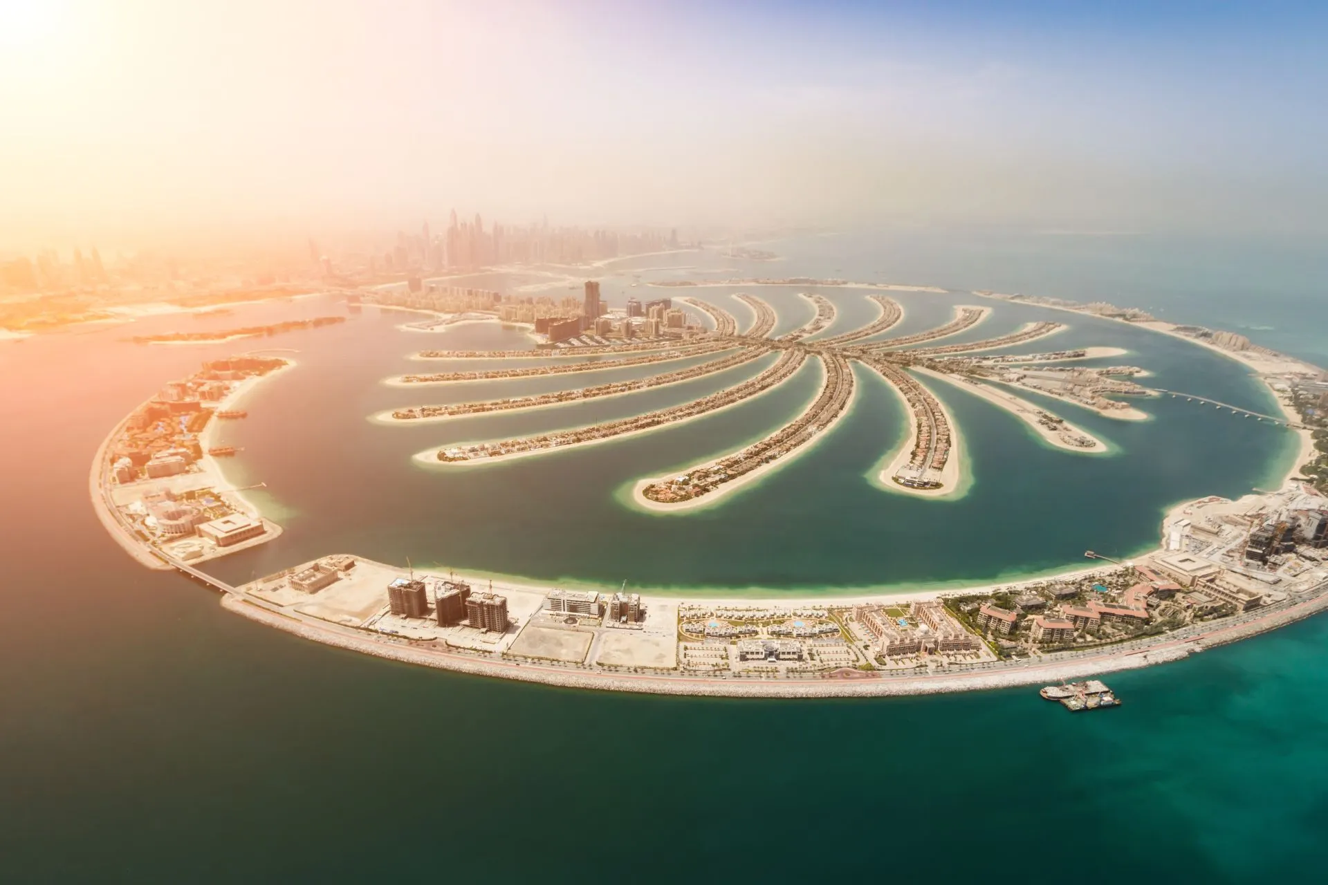 Spectaculair luchtbeeld van Palm Jumeirah in Dubai, een iconisch kunstmatig eiland in de vorm van een palmboom, omringd door helderblauw water en met de skyline van Dubai op de achtergrond. De zon werpt een warme gloed over het landschap, waardoor de moderne architectuur en luxe villa’s op de eilanden prachtig uitkomen. Dit beeld is typerend voor Dubai, een van de beste winterzon bestemmingen voor reizigers die op zoek zijn naar zon, luxe en exotische ervaringen. Terwijl in Europa de winter heerst, biedt deze bestemming een perfecte zonvakantie in december of een zonvakantie in januari, met temperaturen die vaak boven de 25 graden liggen. Voor iedereen die zich afvraagt: waar is het warm in januari? Dubai is het antwoord. Naast indrukwekkende stranden en luxe resorts, vind je hier wereldberoemde bezienswaardigheden, gastronomische hotspots en een bruisend nachtleven. Deze bestemming combineert ontspanning met avontuur, ideaal voor wie wil genieten van zon, cultuur en moderne luxe. Ontdek waarom zoveel reizigers Dubai kiezen als een van de beste winterzon bestemmingen en plan jouw perfecte zonvakantie in december of januari op een locatie waar het altijd warm, zonnig en stijlvol is. Deze foto straalt elegantie, exotische charme en ultieme vakantiesfeer uit – alles wat je zoekt voor een onvergetelijke winterzon ervaring.

