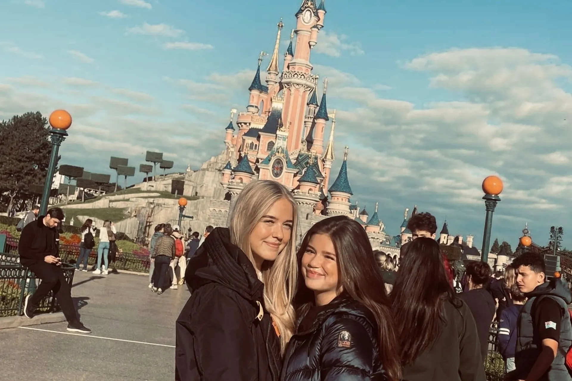 Twee bezoekers poseren op Main Street in Disneyland Parijs met het iconische Doornroosje kasteel op de achtergrond en een heldere blauwe lucht.