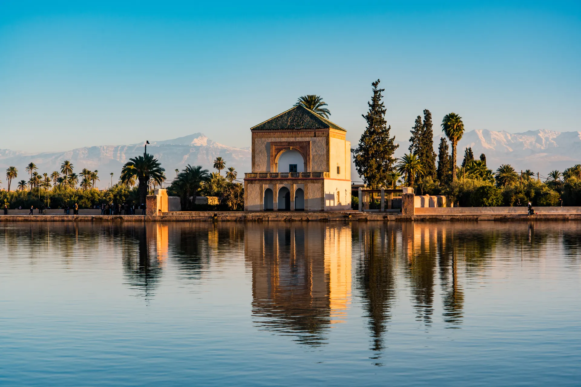 Historisch gebouw Menara-paviljoen in Marrakech, Marokko, weerspiegeld in een rustige vijver met palmbomen en de besneeuwde toppen van het Atlasgebergte op de achtergrond. Iconische bezienswaardigheid in een serene omgeving, ideaal voor cultuur, fotografie en reizen. Ontdek Marokkaanse architectuur, exotische tuinen, traditionele charme en indrukwekkende landschappen in Marrakech.