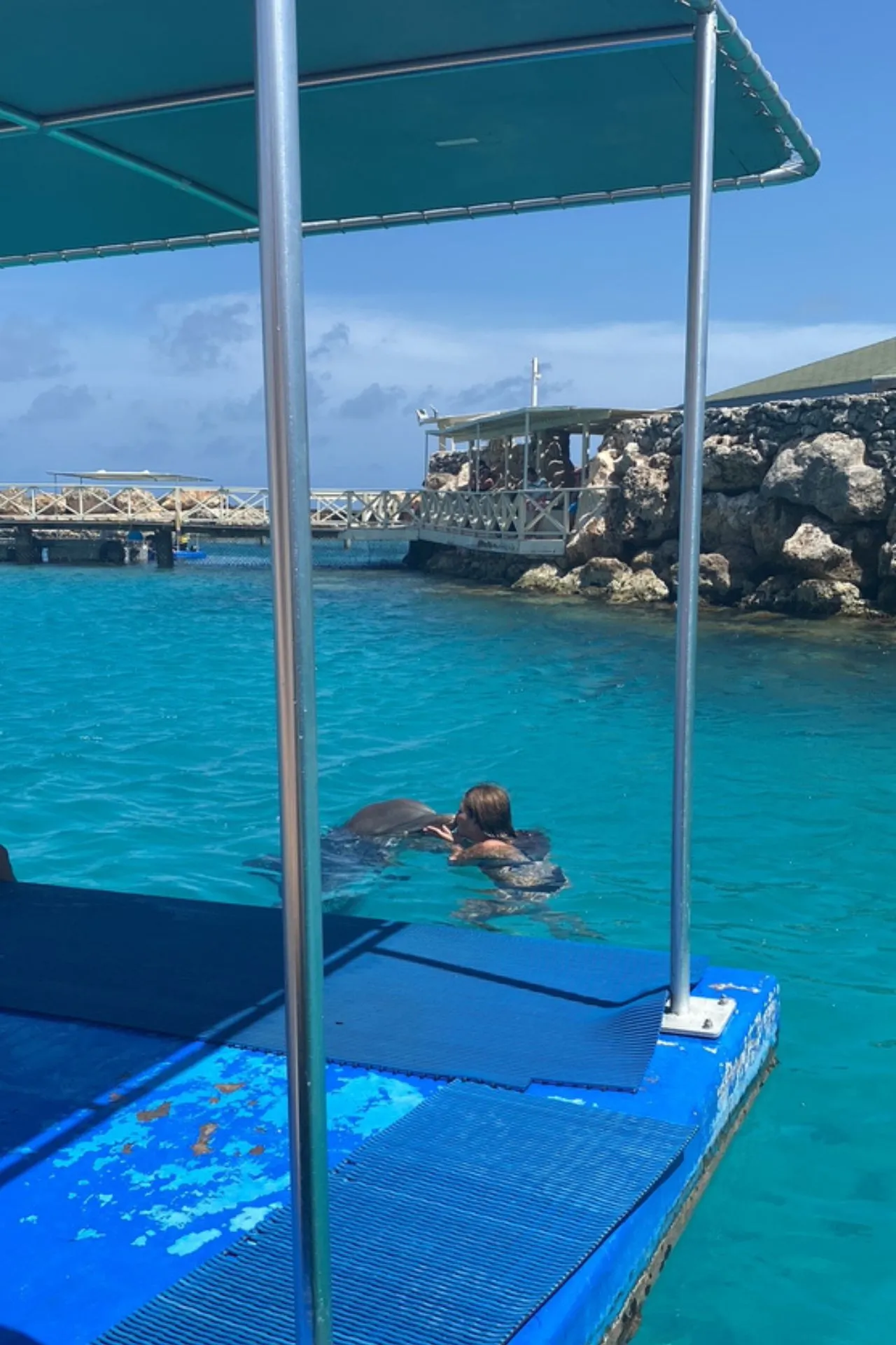 Zwemmen in het helder turquoise water van Curaçao, omringd door een steiger en rotsen. Een unieke ervaring op het eiland waar ontspanning en bijzondere activiteiten samenkomen aan zee.
