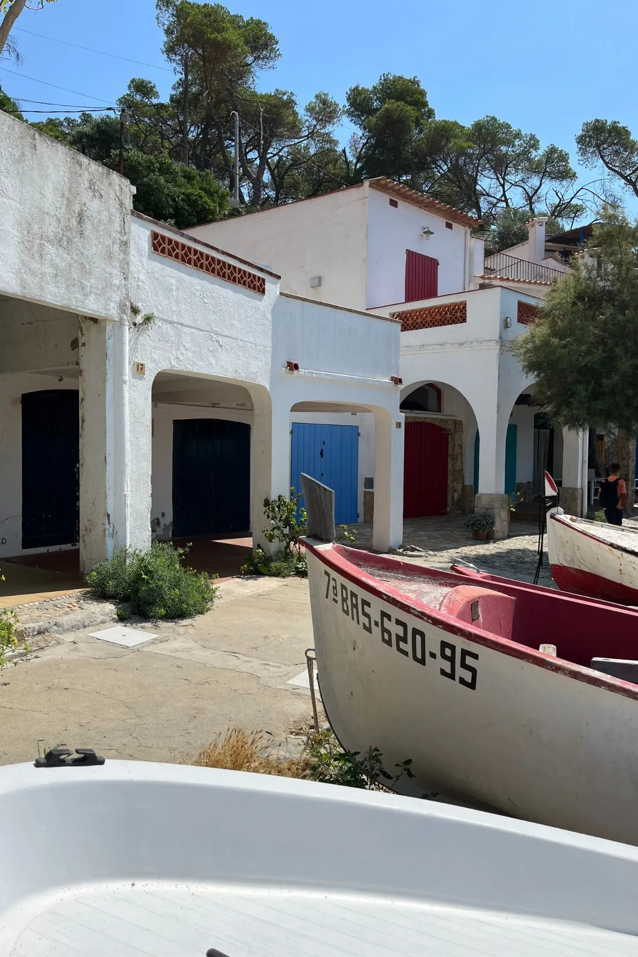 Traditionele witte huizen met gekleurde deuren en luiken, een rode boot op de voorgrond, gelegen in een zonnige kustplaats.
