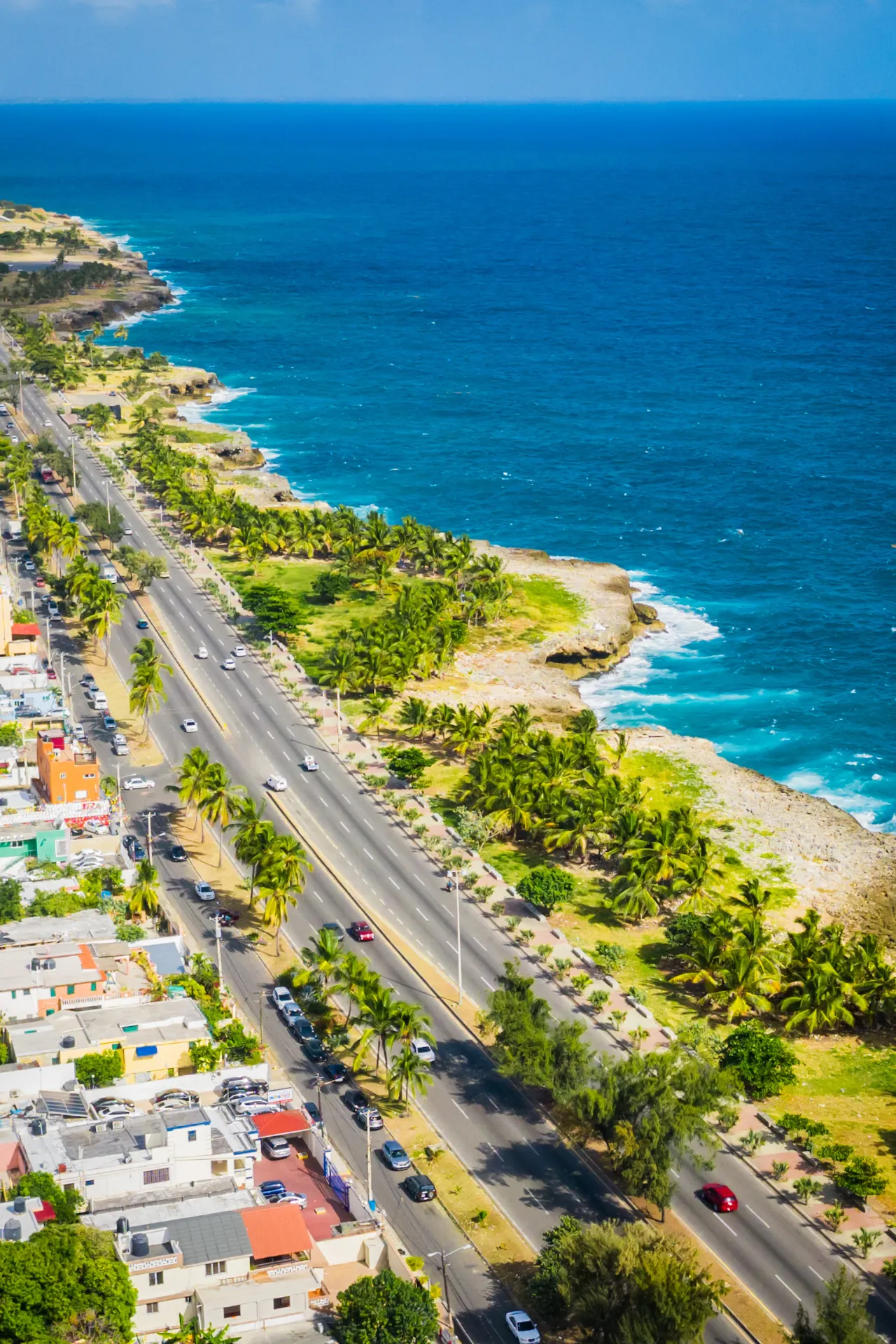 Luchtfoto van Santo Domingo met een asfaltweg die langs de kustlijn loopt, omringd door blauw zeewater en stedelijke bebouwing.