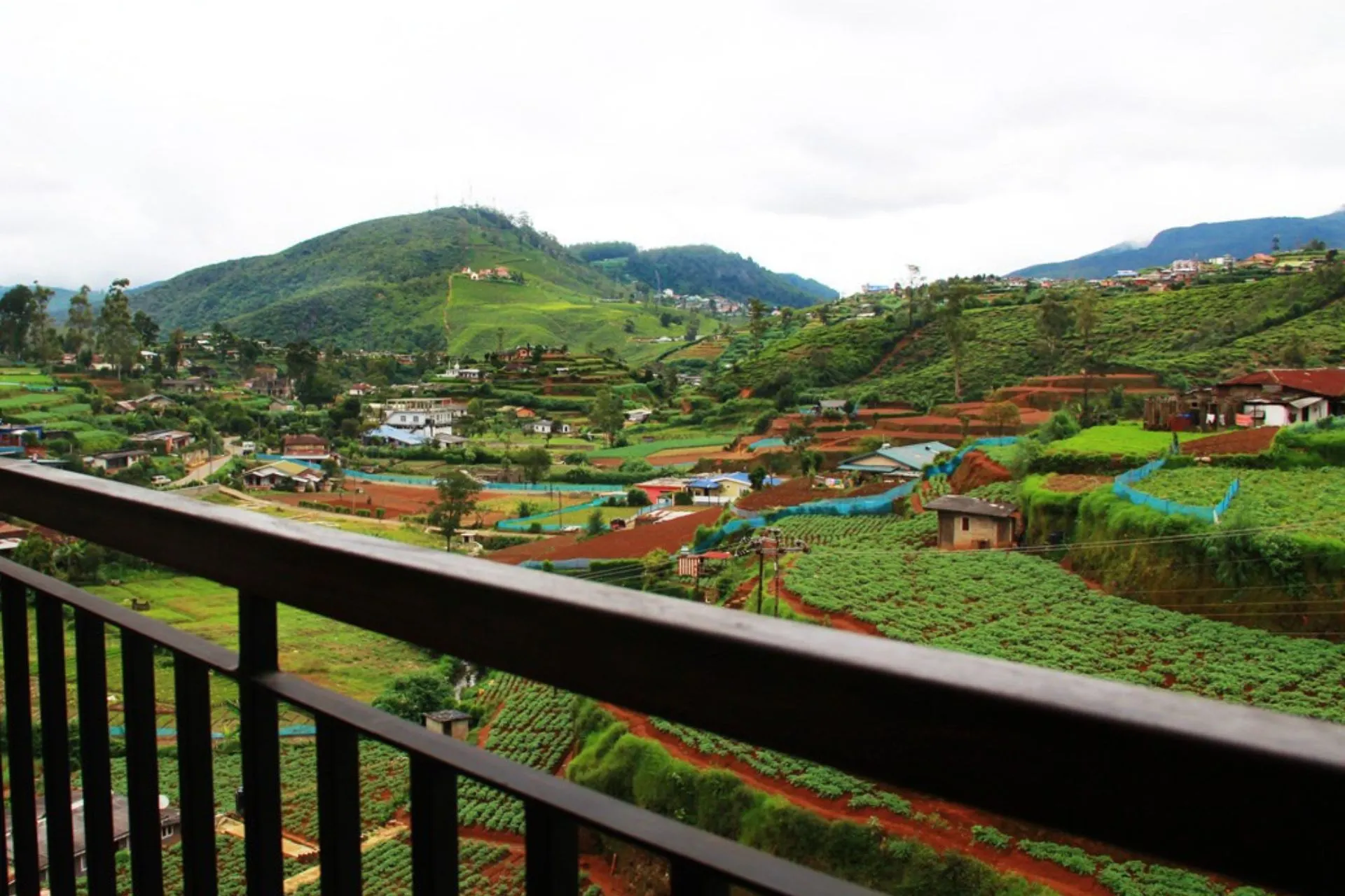 Uitzicht vanaf het balkon van The Blackpool Hotel Nuwara Eliya over groene heuvels, landbouwterrassen en verspreid liggende huizen in het berglandschap van Sri Lanka.