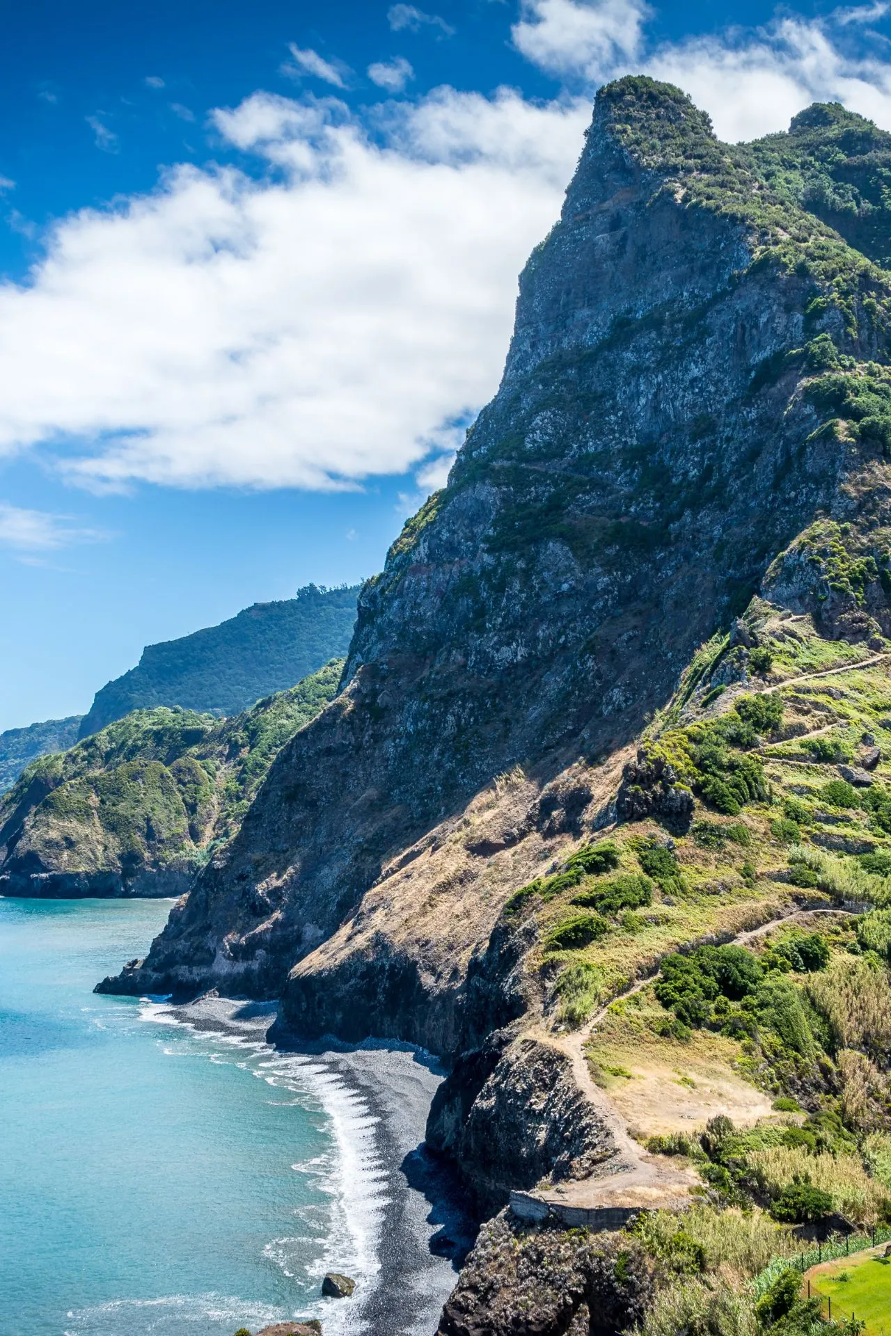 Spectaculair uitzicht op een imposante rotsformatie langs een kustlijn met helderblauw water en groene vegetatie. De lucht is helder met enkele wolken, wat een zonnige en warme sfeer creëert. Dit beeld is typerend voor Madeira, een van de beste winterzon bestemmingen voor reizigers die op zoek zijn naar zon, natuur en avontuur. Terwijl in Europa de winter heerst, biedt deze plek een perfecte zonvakantie in december of een zonvakantie in januari, met aangename temperaturen en volop zon. Voor iedereen die zich afvraagt: waar is het warm in januari? Madeira is het antwoord. Ontdek waarom zoveel reizigers deze plek kiezen als een van de beste winterzon bestemmingen en plan jouw perfecte zonvakantie in december of januari op een locatie waar het altijd warm en gastvrij is.
