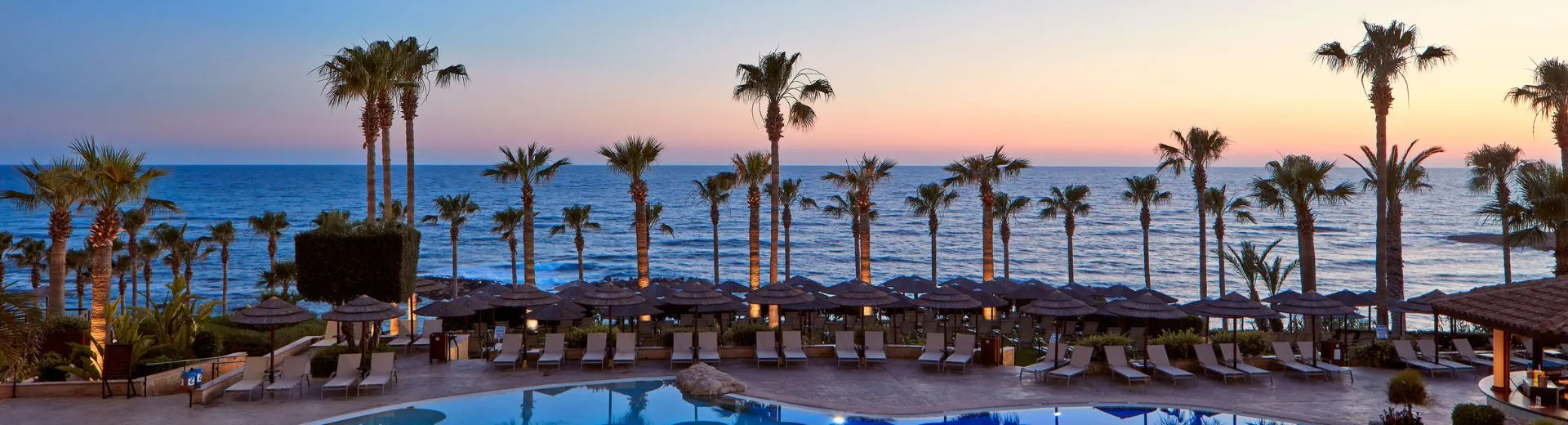 Uitzicht op zee vanaf een Atlantica resort bij zonsondergang - Luxe Atlantica resort met palmbomen en zwembad aan zee tijdens zonsondergang