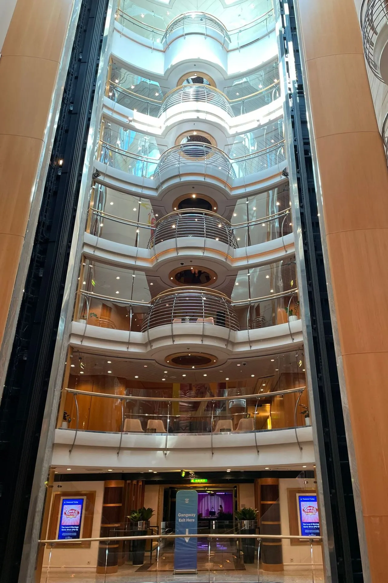 Hoog atrium van de Independence of the Seas met meerdere verdiepingen en glazen liften, omringd door moderne balustrades en warme houten accenten.