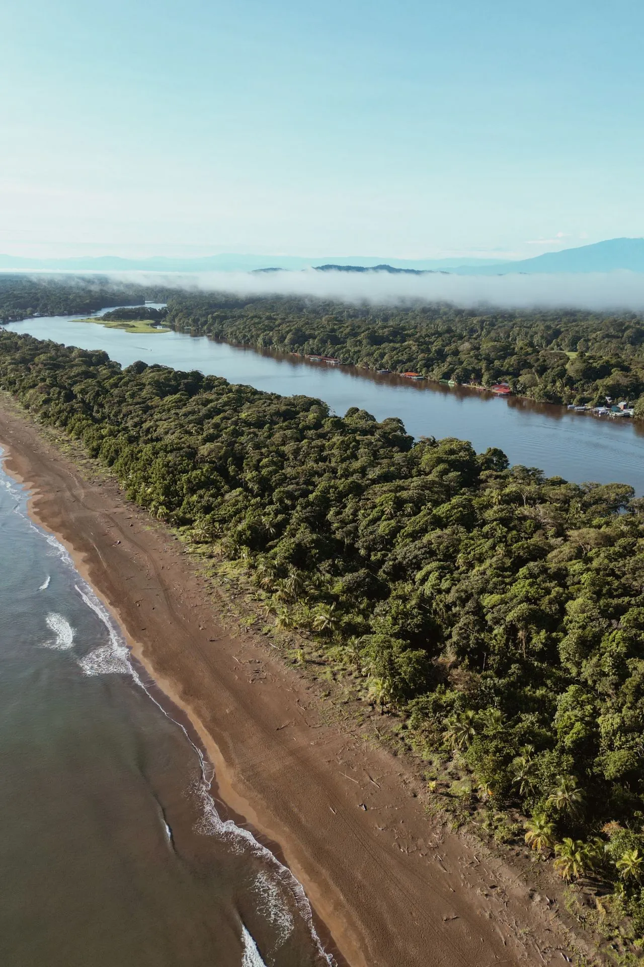 Luchtfoto van een tropisch strand en rivier in Tortuguero, Costa Rica, met mist over het regenwoud.
