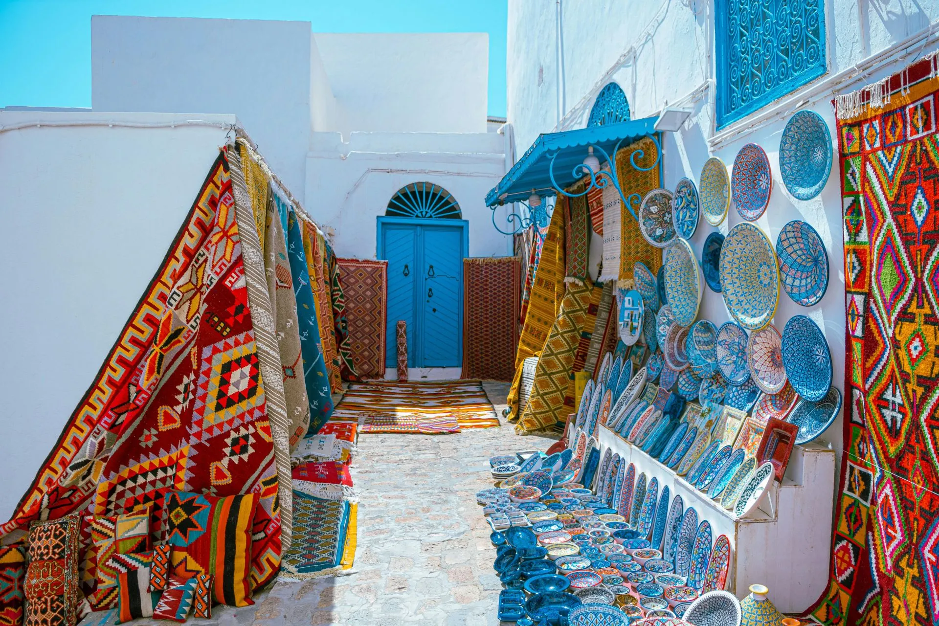 Traditionele marktstraat in Sidi Bou Said, een van de mooiste plaatsen van Tunesië. Tussen witgekalkte gebouwen met karakteristieke blauwe deuren en ramen worden kleurrijke tapijten, keramiek en lokale ambachten verkocht. Dit sfeervolle kunstenaarsdorp nabij Tunis staat bekend om zijn authentieke charme en mediterrane uitstraling.