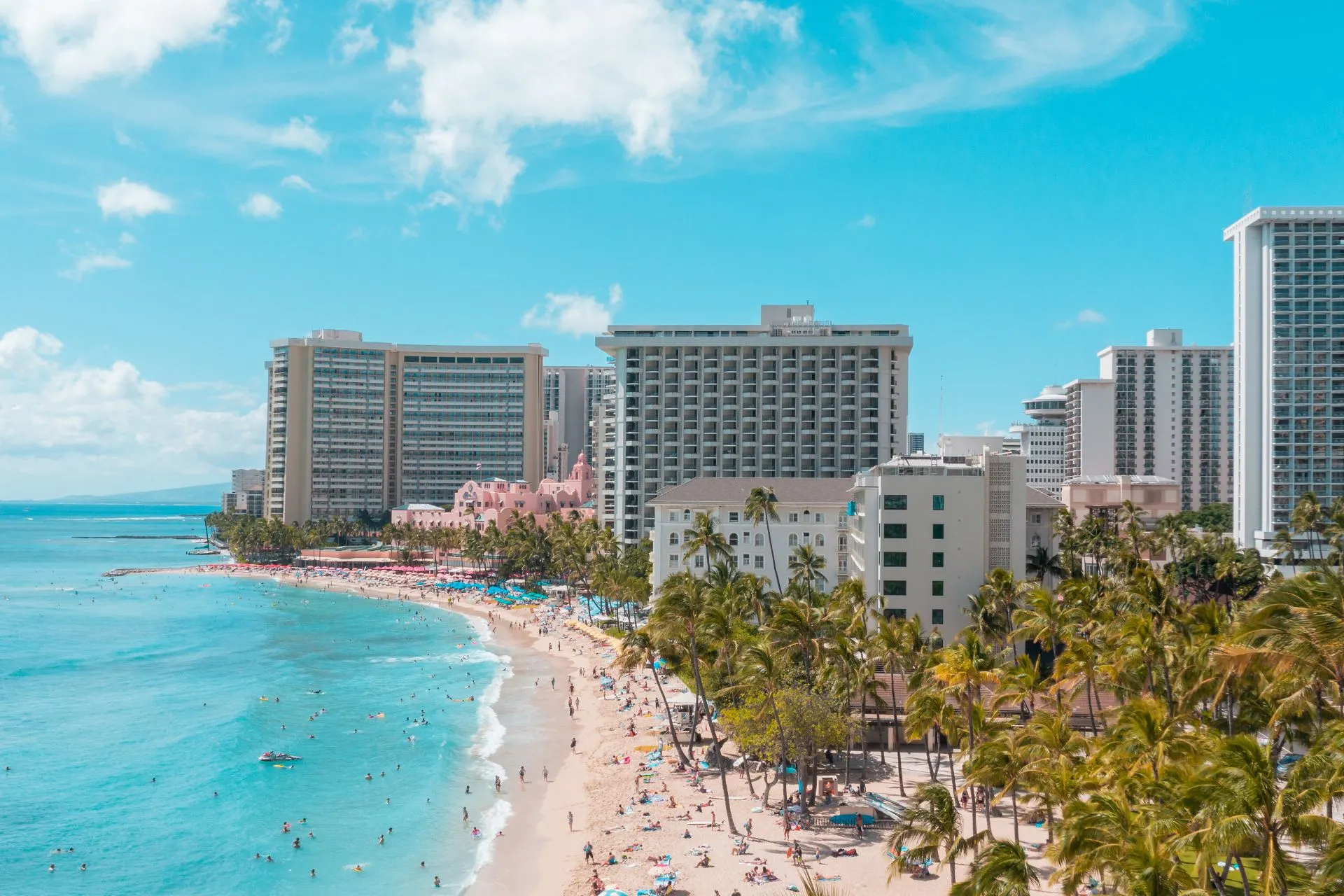 Panorama van Waikiki Beach met helderblauwe oceaan, hoge hotels en palmbomen.