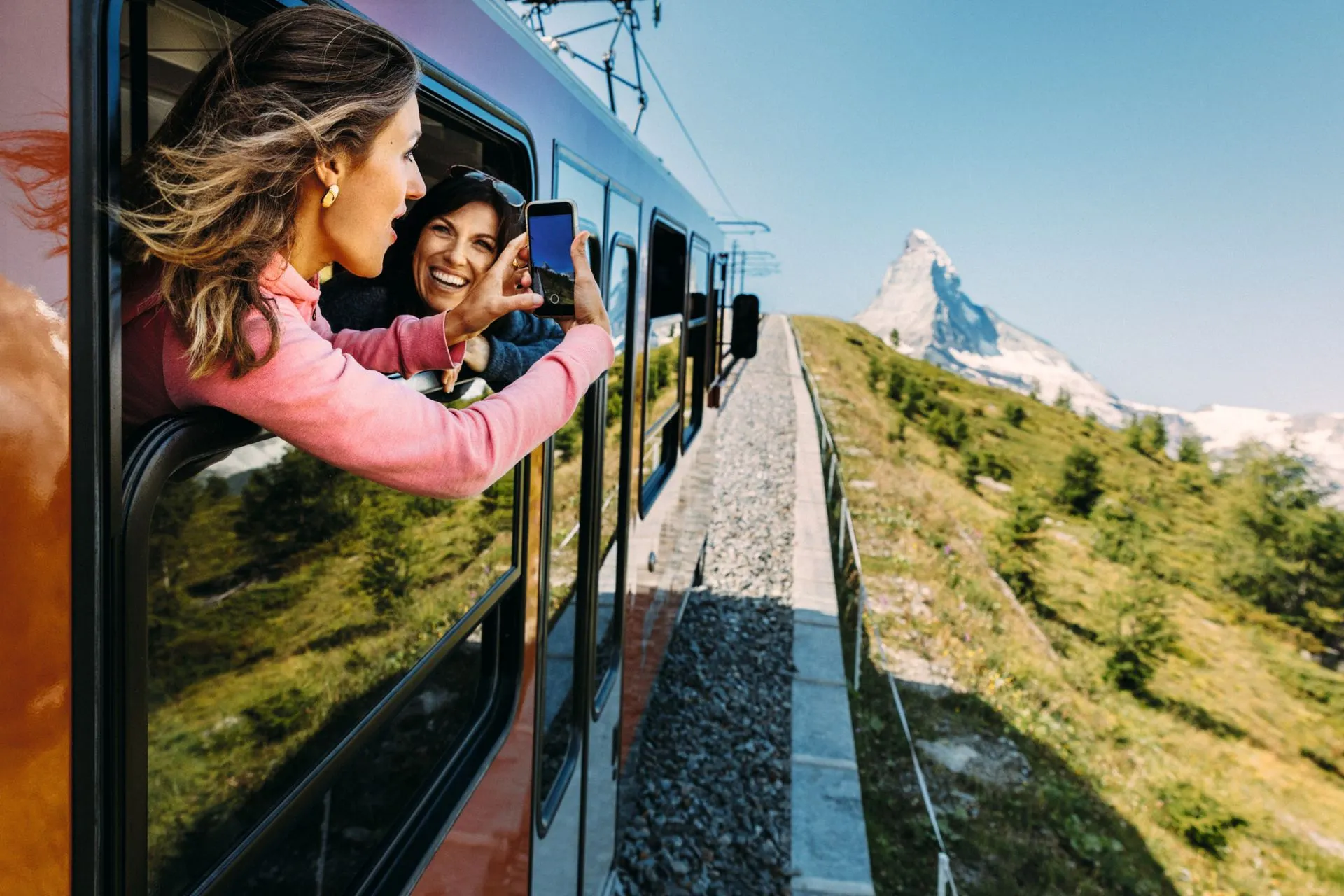 Twee vrouwen steken hun hoofden uit het treinraam en maken een selfie terwijl de iconische Matterhorn zichtbaar is op de achtergrond